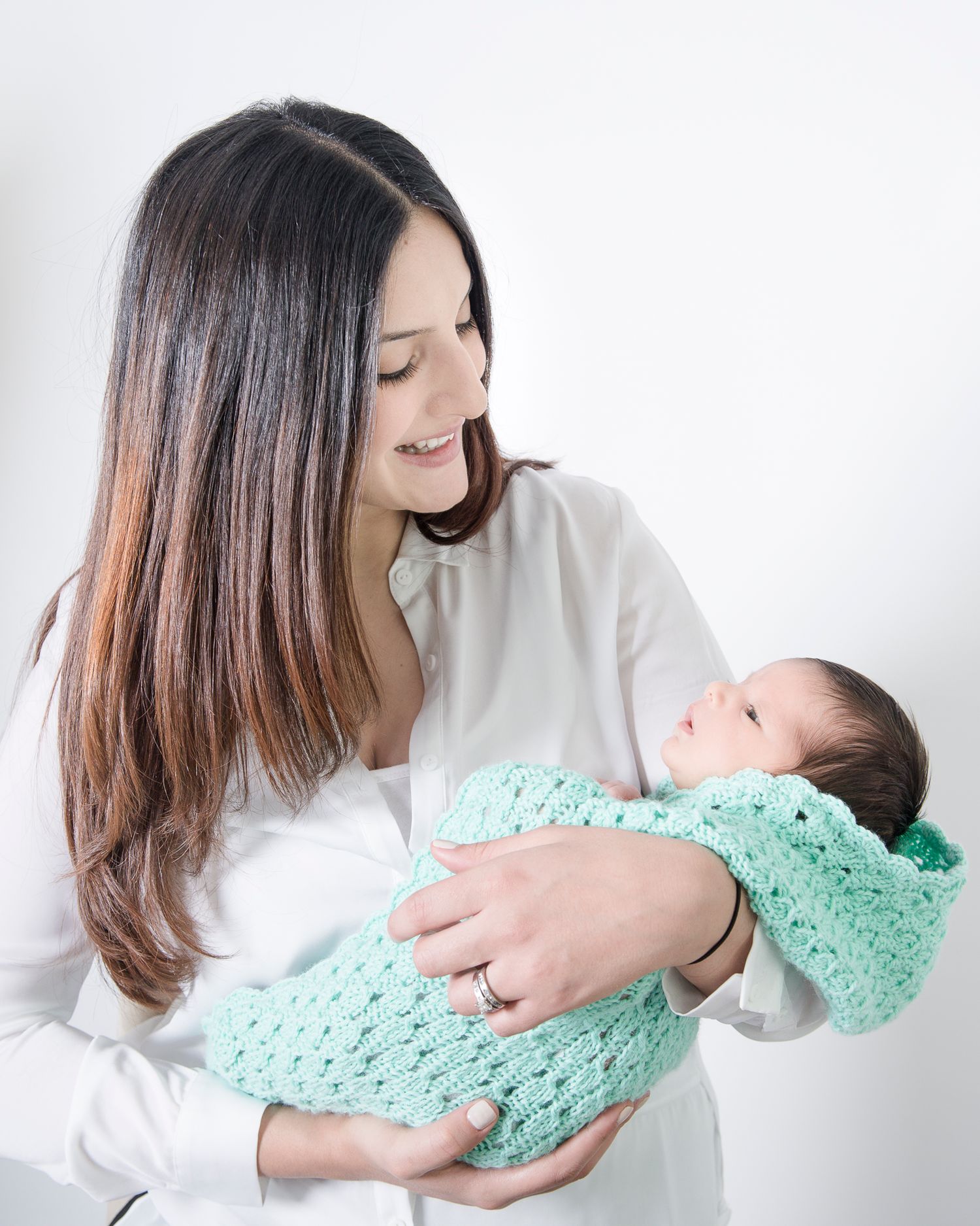 Parent in white shirt cradling newborn wrapped in mint green knit blanket.