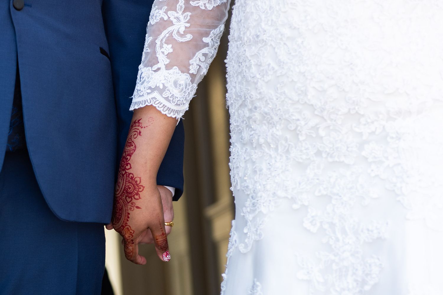 A couple in formal wedding attire stands together, with the bride wearing white lace and groom in navy blue suit.