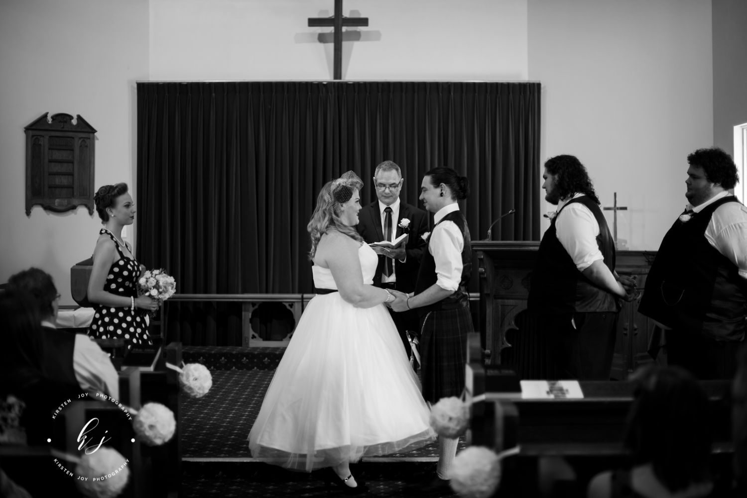 A couple during their wedding ceremony as guests look on in black and white.