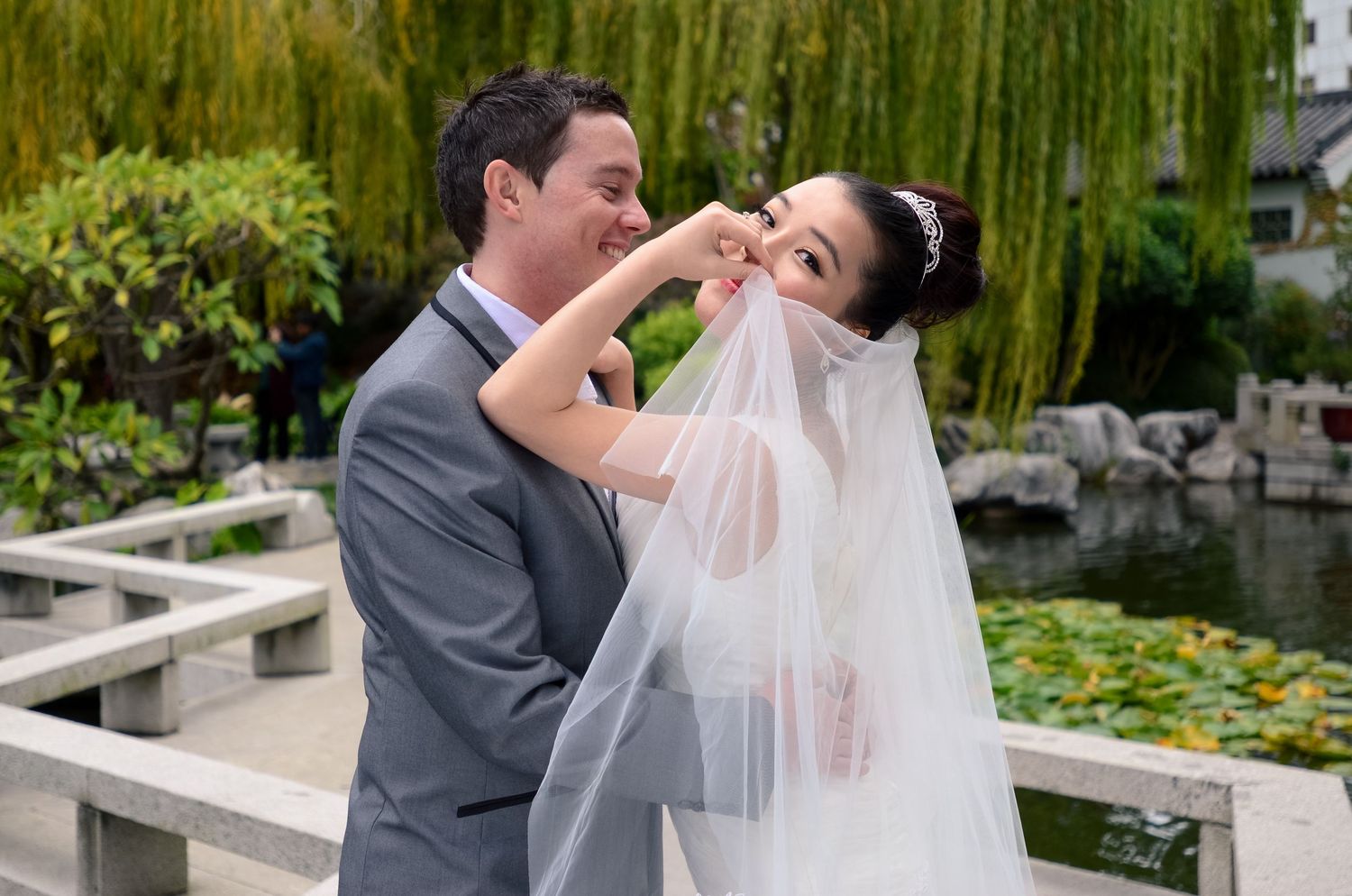 Romantic garden wedding scene with couple embracing near bamboo plants.