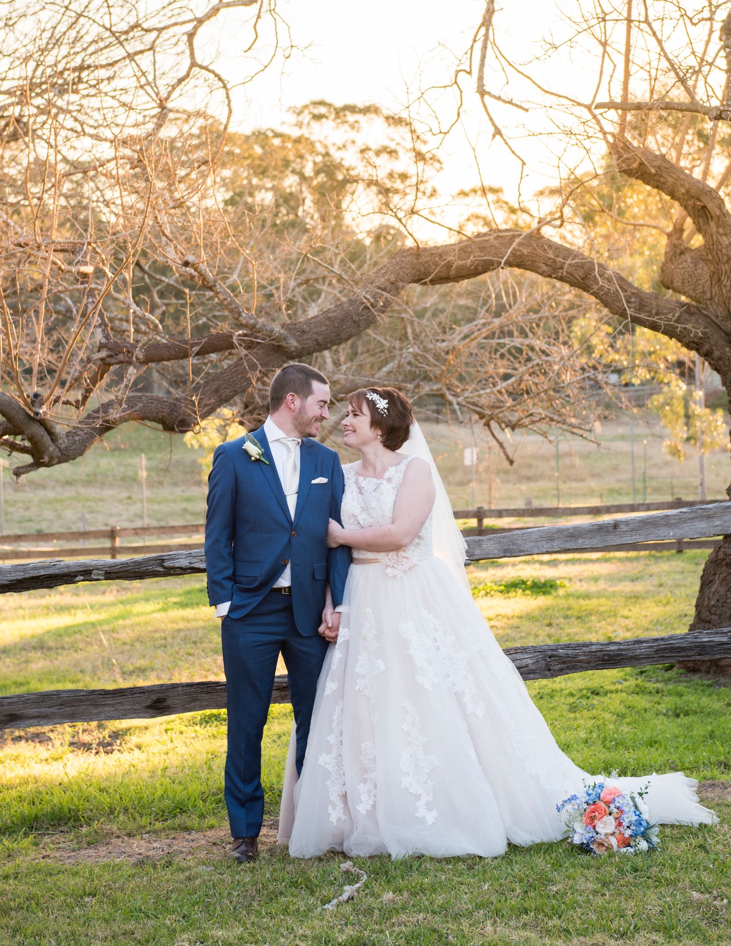 Romantic outdoor wedding portraits under sprawling tree branches at sunset.
