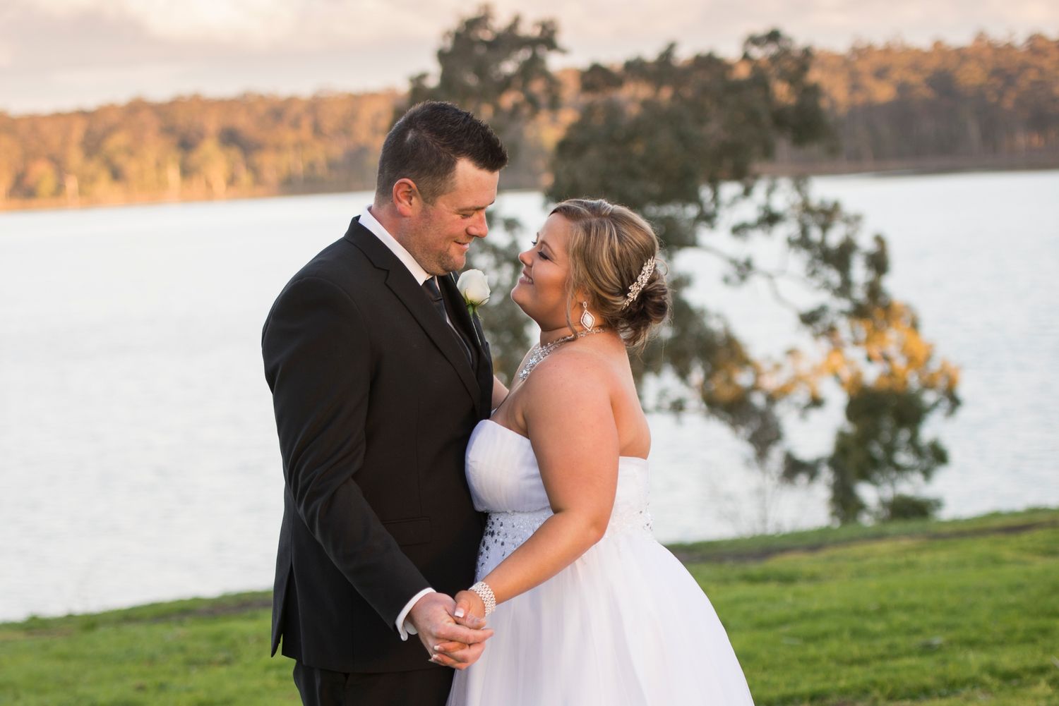 Newlywed couple shares romantic moments during sunset by a serene lakeside setting.