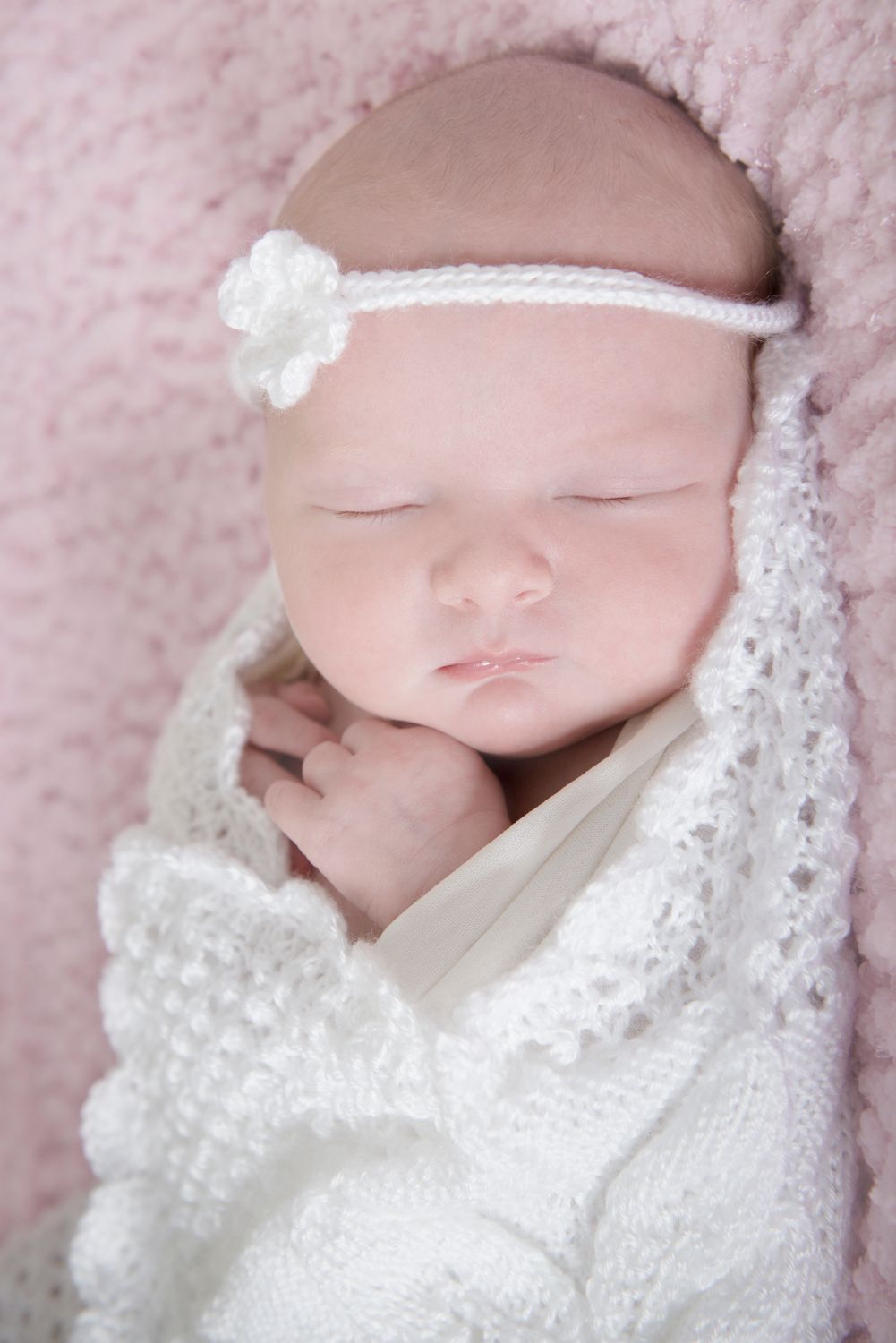 Newborn wrapped in delicate white lace blanket sleeping peacefully.