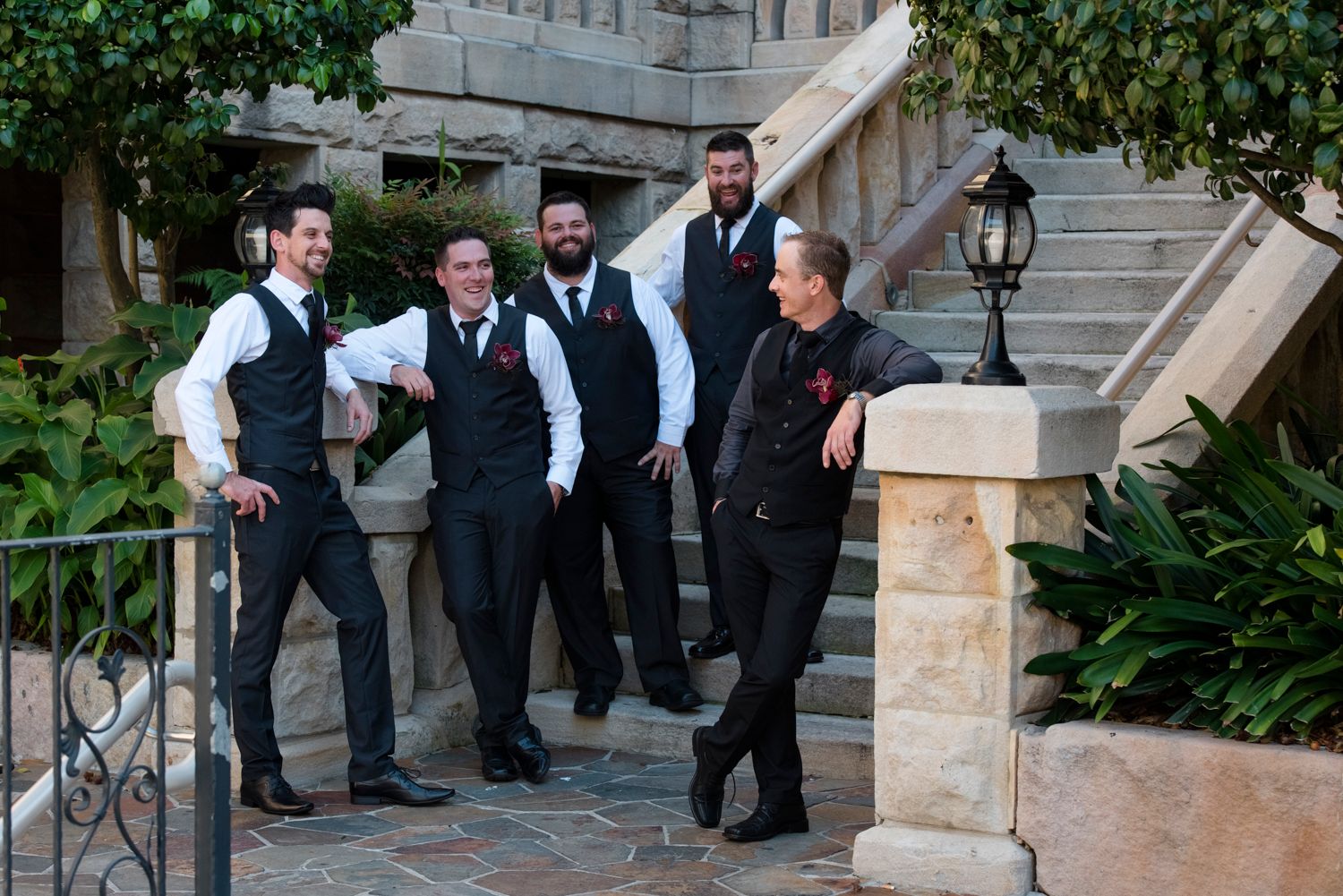 A group of people in formal attire gathered on outdoor stone steps with greenery visible in the background.
