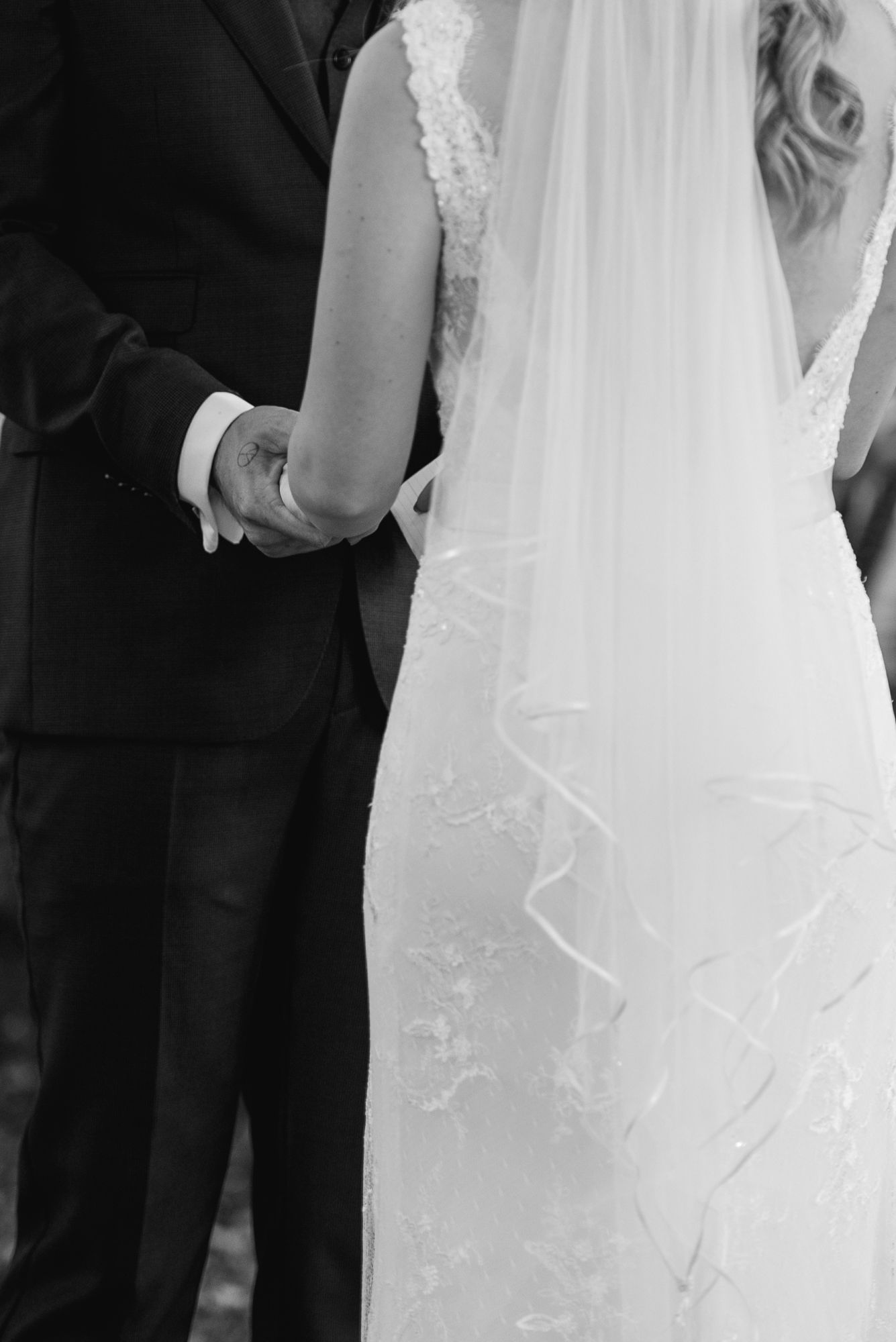 Close-up view of a bride and groom standing together in formal wedding attire showing partial details of dress and suit.