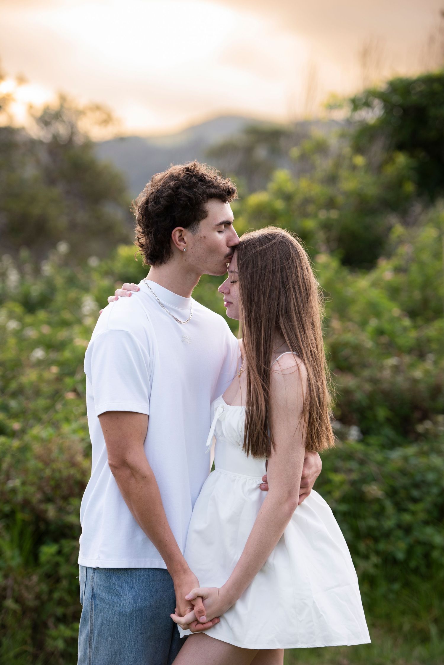 A couple in white top and jeans and white dress share romantic moments in a series of outdoor photos at sunset.
