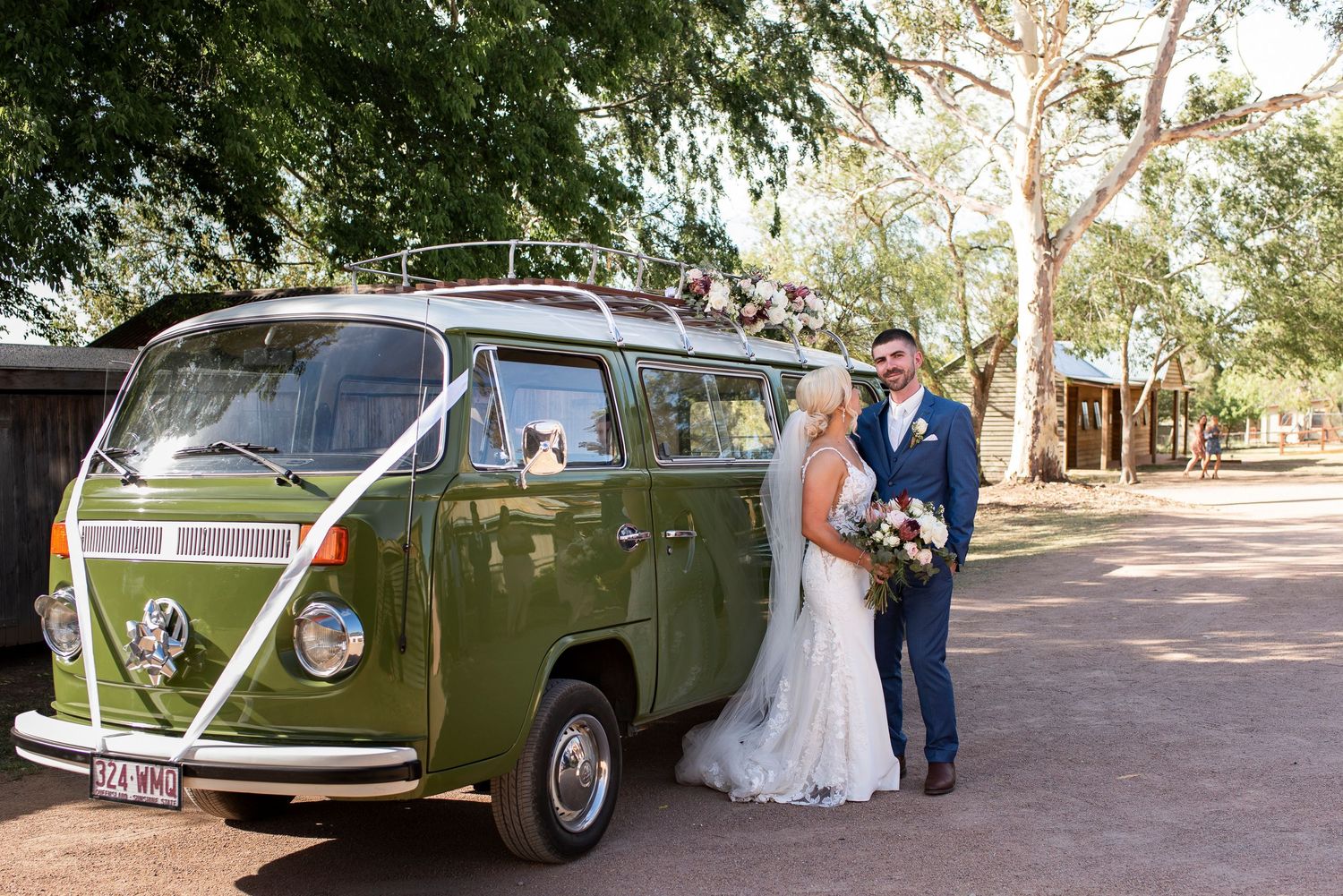 Newlyweds pose beside a vintage green Volkswagen van decorated with wedding ribbons.