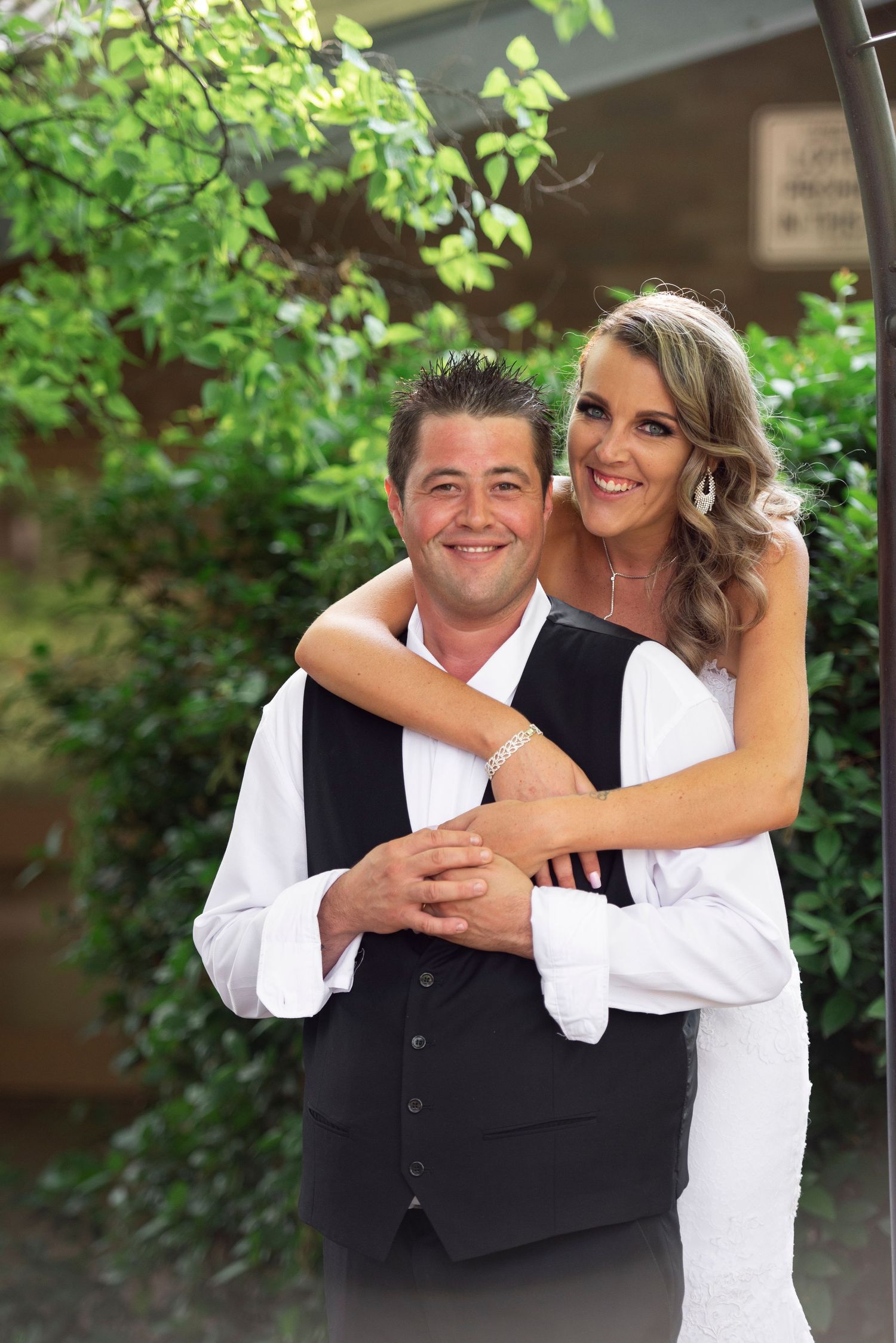 A couple shares a joyful embrace outdoors with green foliage in the background.