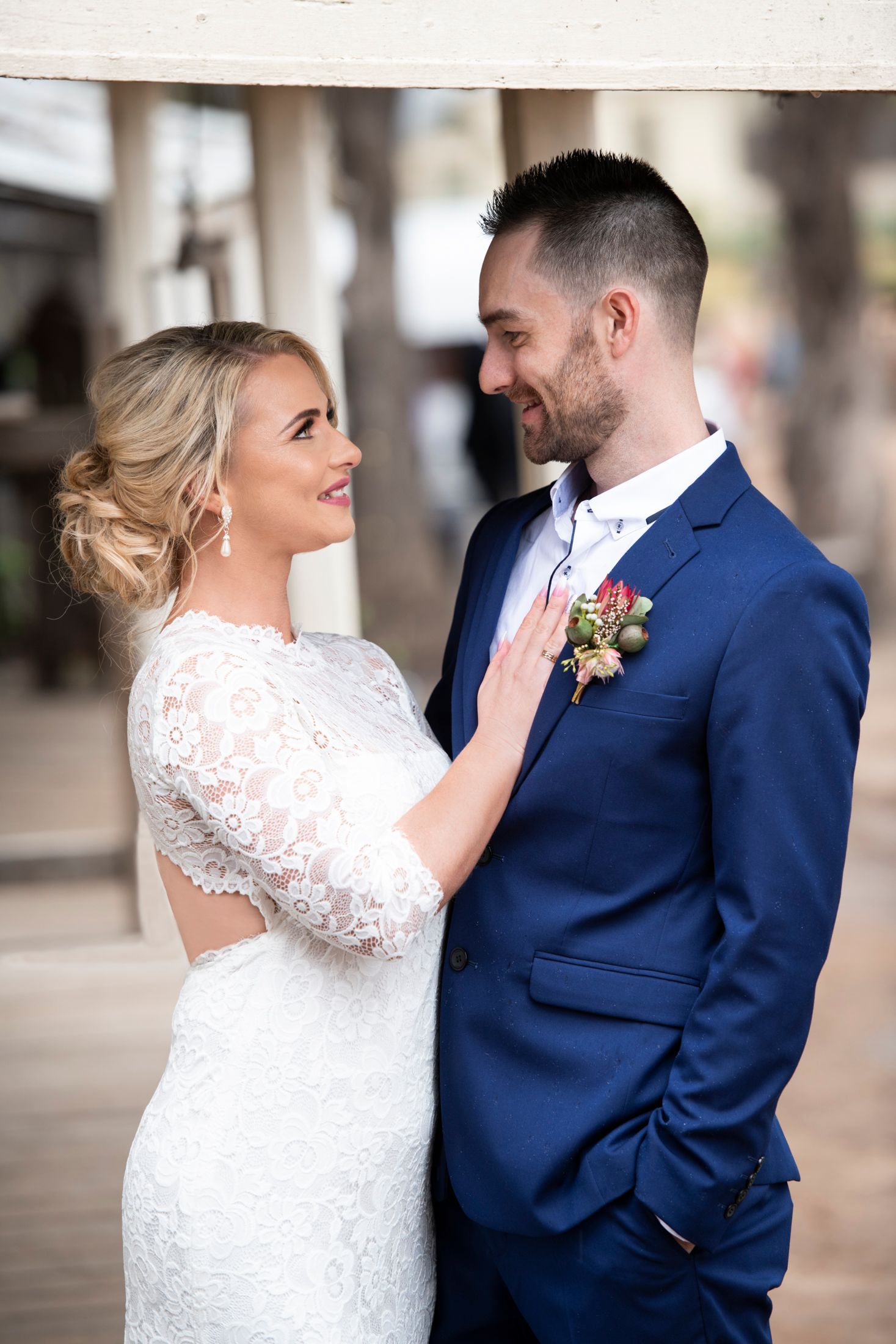 A bride in white lace dress and groom in navy suit share an intimate moment during their wedding photoshoot.