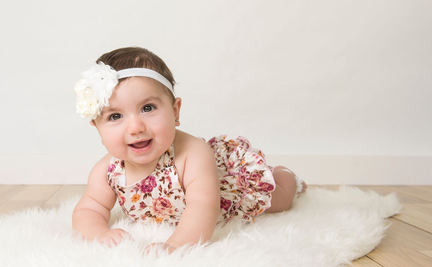 Baby in floral outfit lies on soft white blanket during photo session.