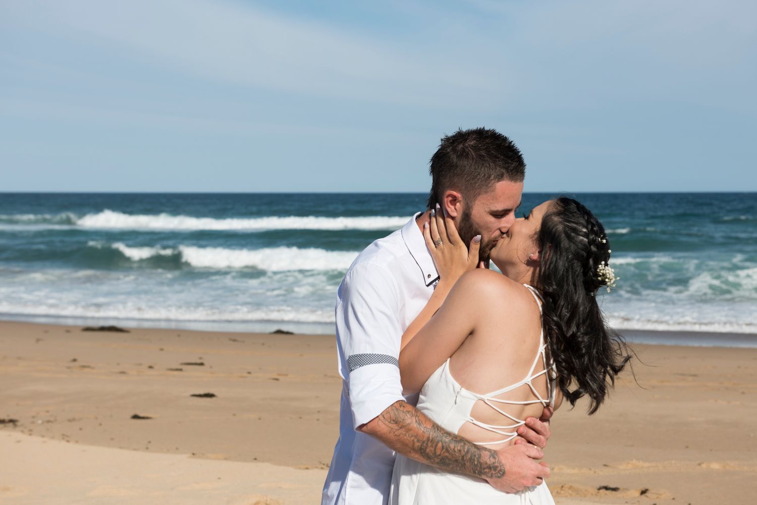 Romantic wedding photo series showing couple embracing on sandy beach with ocean waves in background.