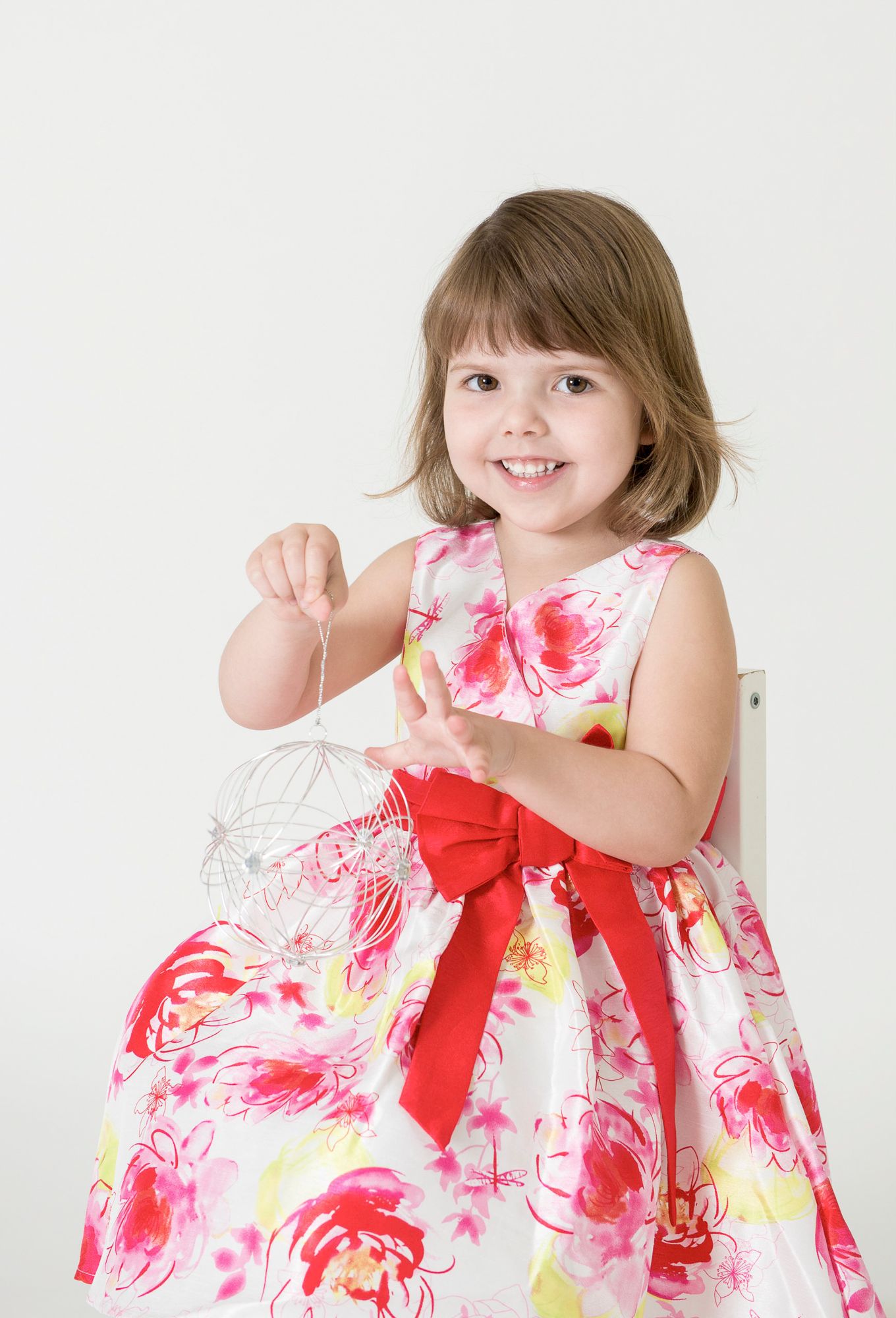 Child twirls in pink and white floral dress with red bow during studio session.