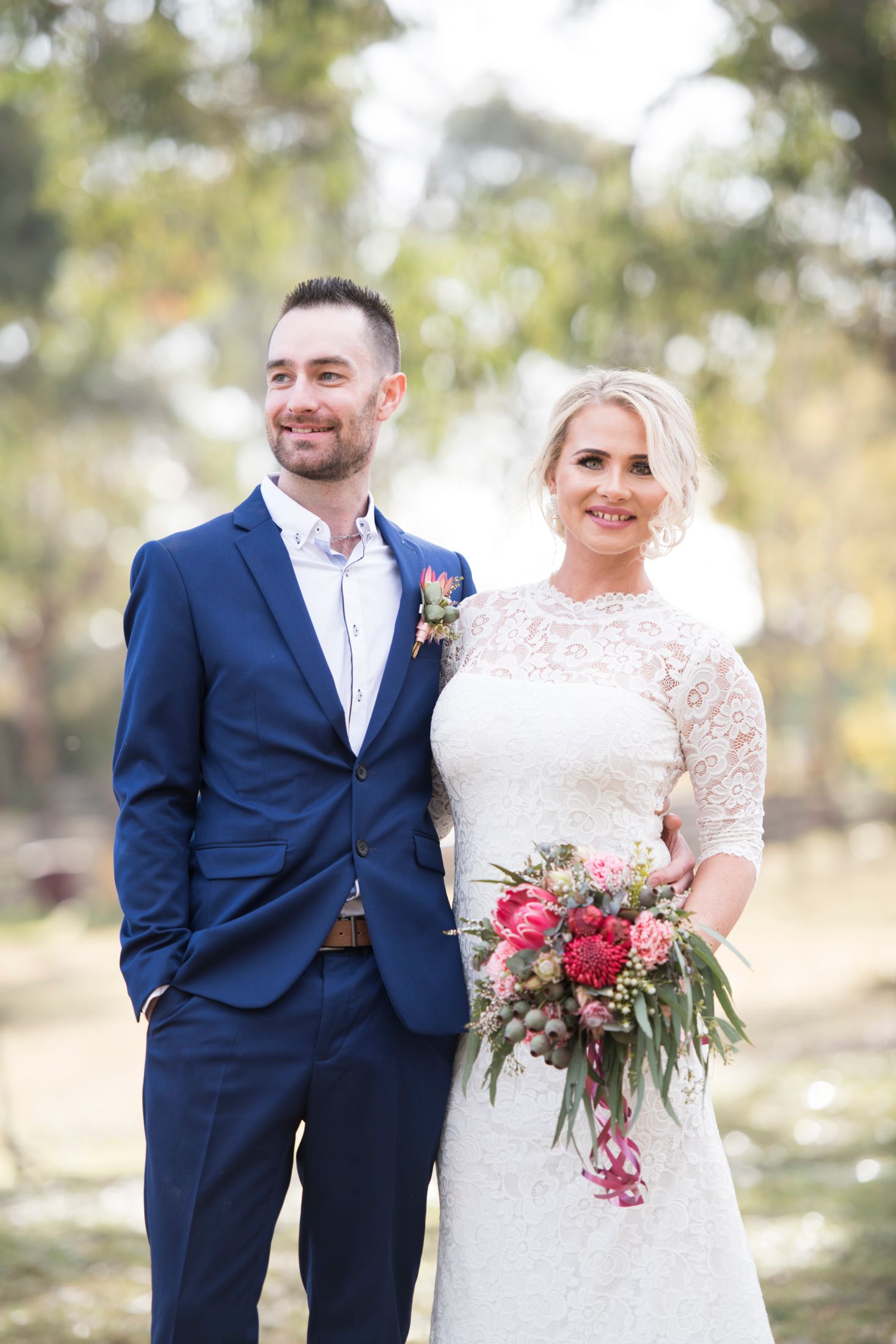 A bride and groom share a joyful moment together outdoors in a natural setting with blurred bokeh background.