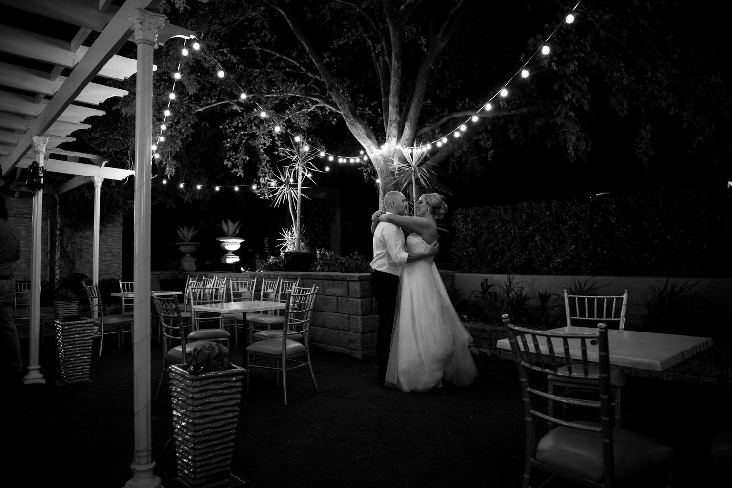 A romantic outdoor reception venue at night with string lights illuminating an empty dance floor and chairs.