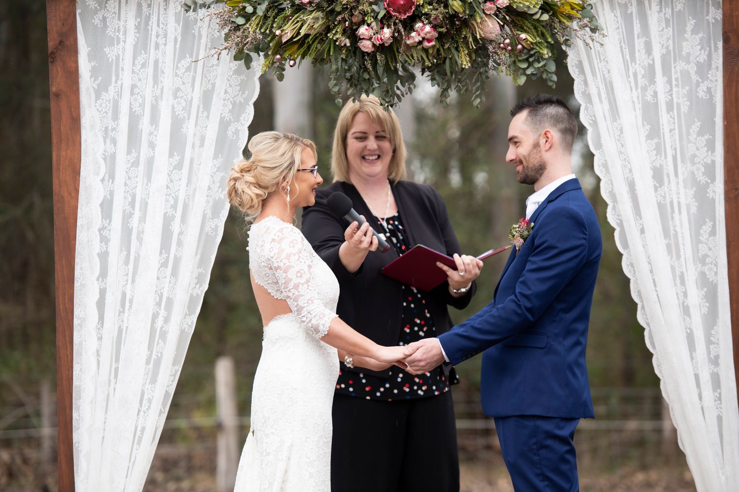 A romantic wedding ceremony takes place under white lace curtains in an outdoor country setting.