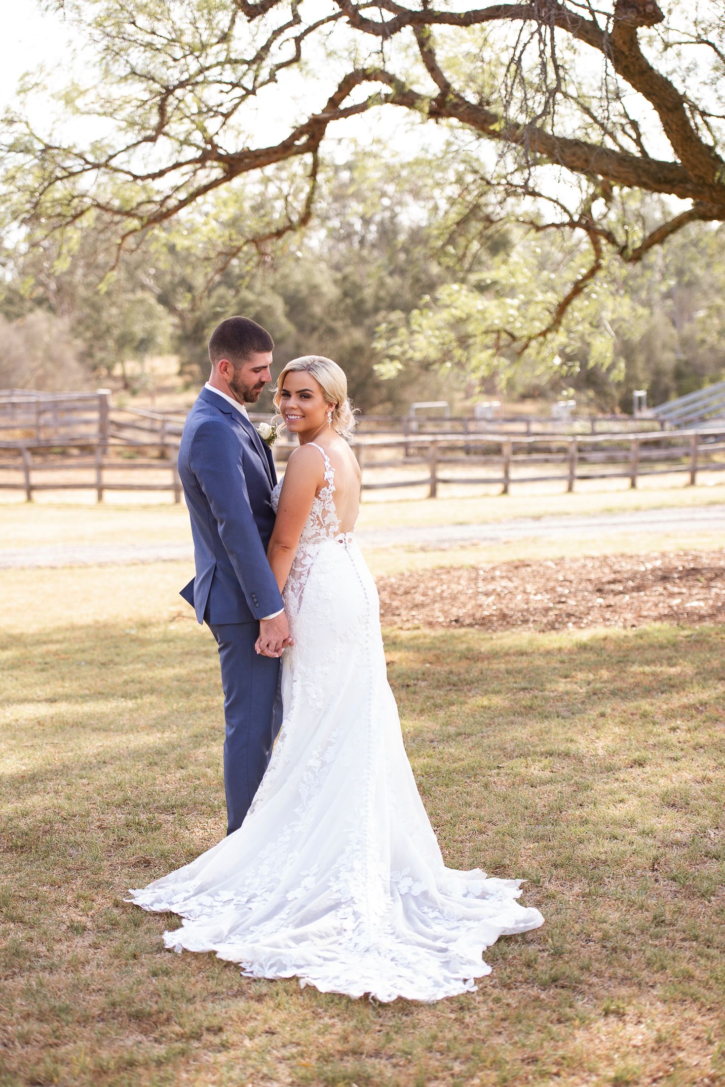 Sunlit portrait of a couple in wedding attire standing beneath a majestic oak tree.