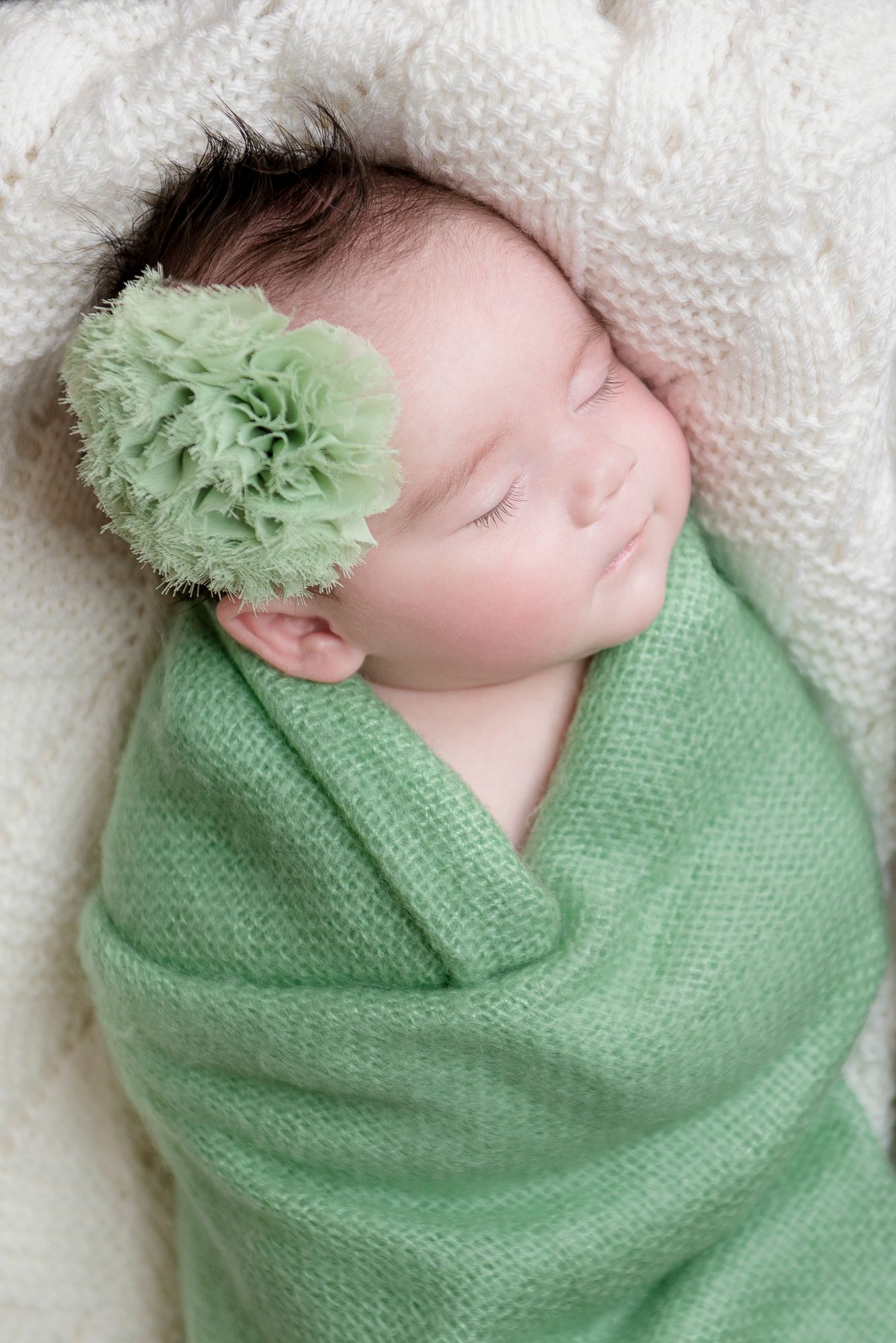 Sleeping baby wrapped in mint green knit blanket with matching bow accessory.