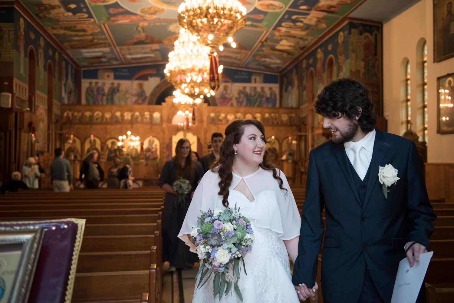 A wedding ceremony in an ornate church with chandeliers and painted murals on the ceiling.