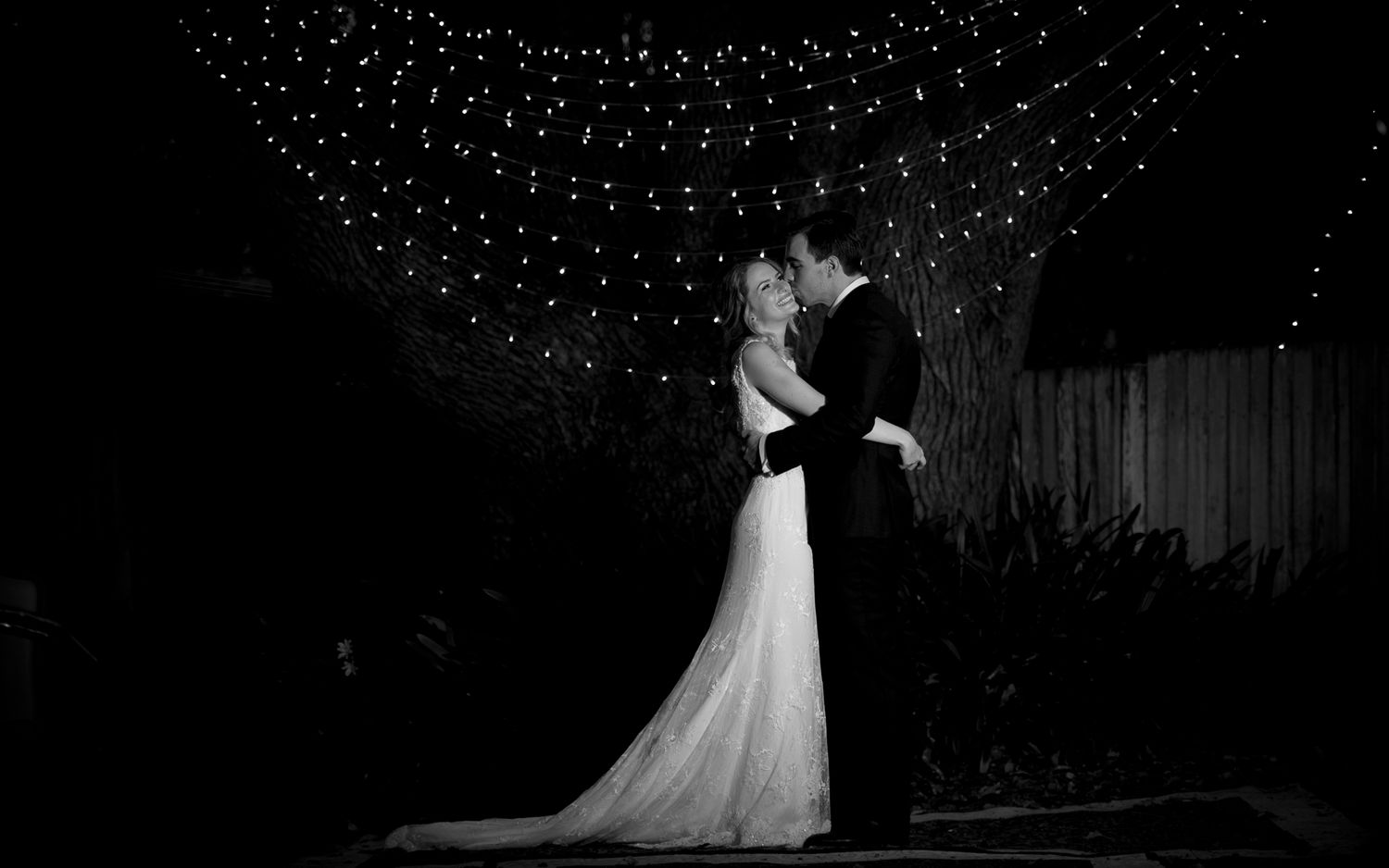 Romantic silhouette of a couple dancing at a wedding reception under twinkling lights.