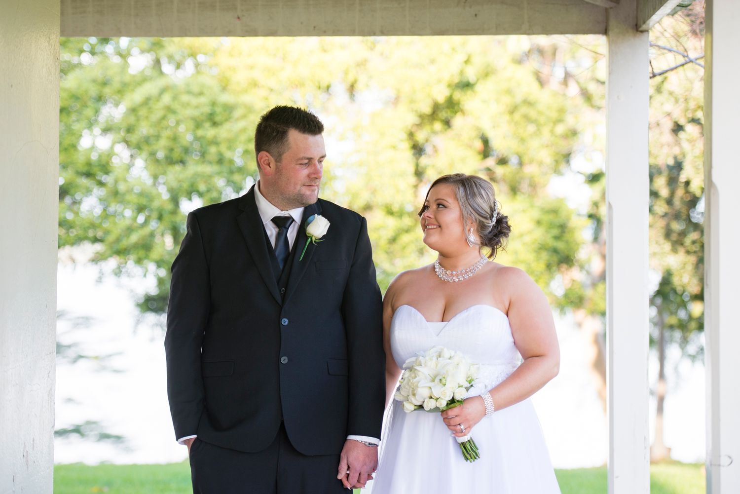 A bride and groom share a tender moment together under a white covered porch on their wedding day.