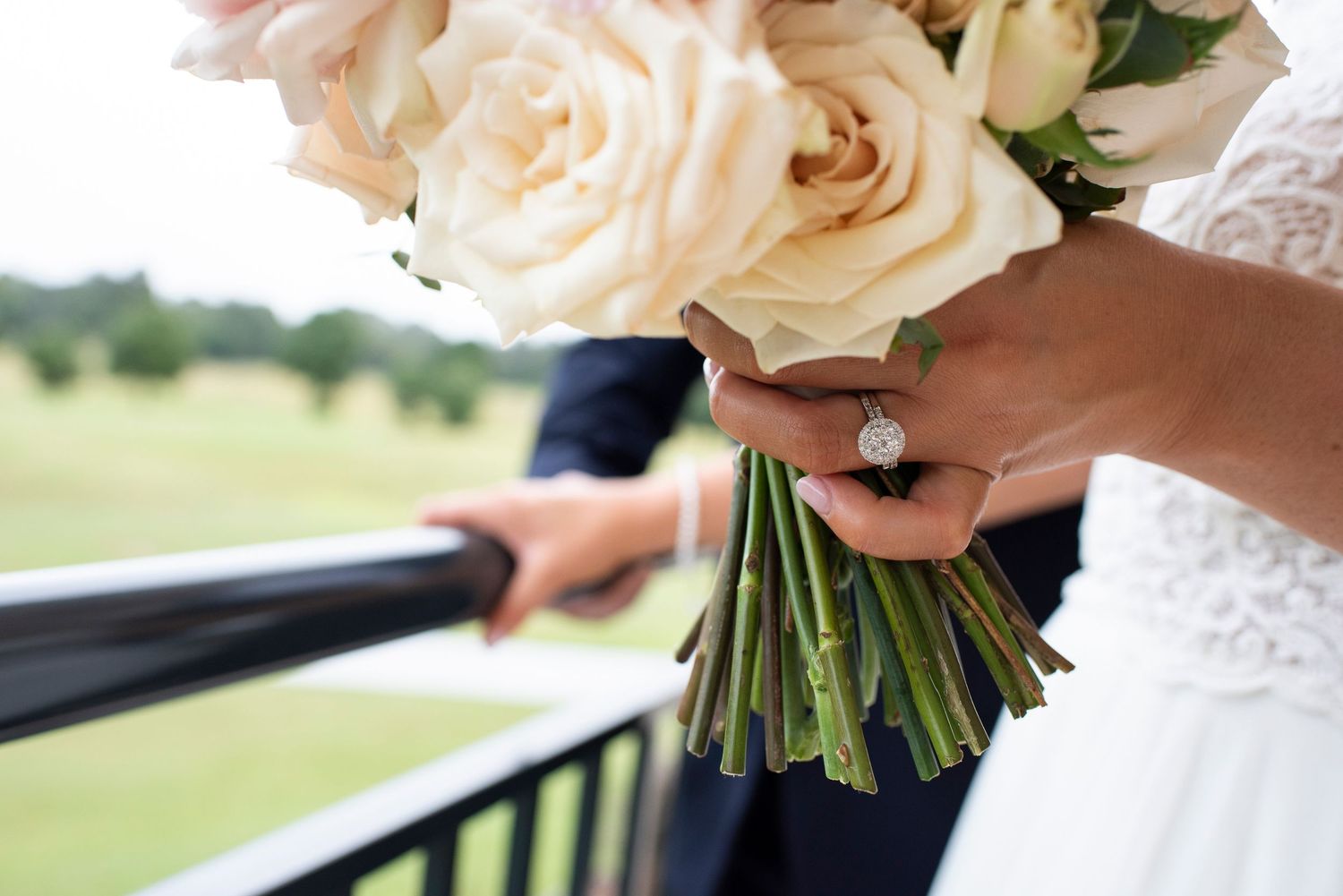 Elegant white rose and greenery wedding bouquet held against a white dress with lace detail.