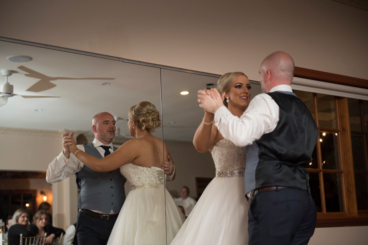 Couples share a dance together at an elegant wedding reception in a banquet hall with warm lighting.