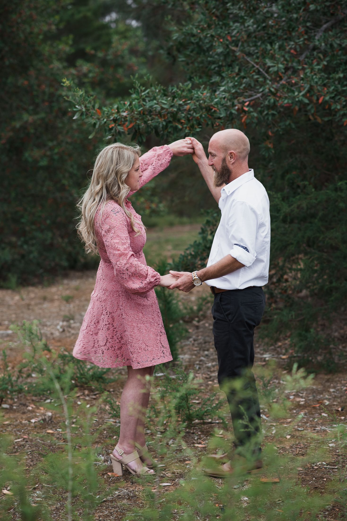 A couple dancing and embracing in a natural outdoor setting with green foliage.