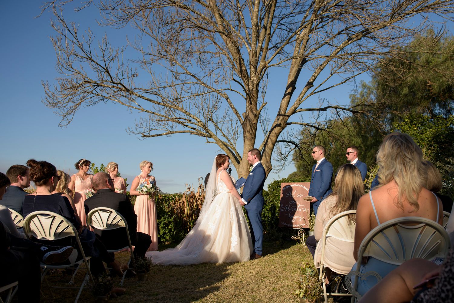 Wedding guests seated on a grassy hillside during an outdoor ceremony.