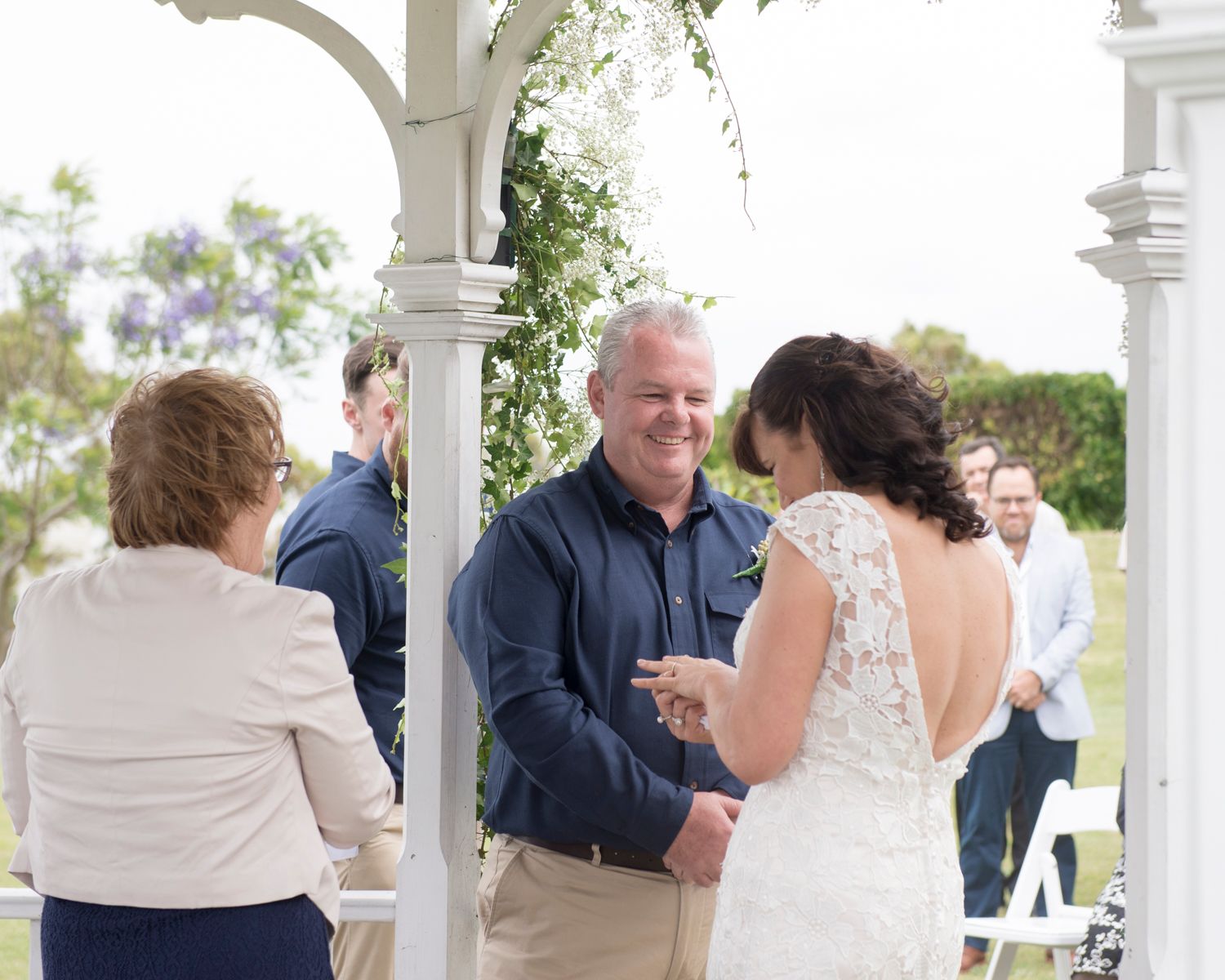 Wedding guests gather under a white pergola during an outdoor reception celebration.