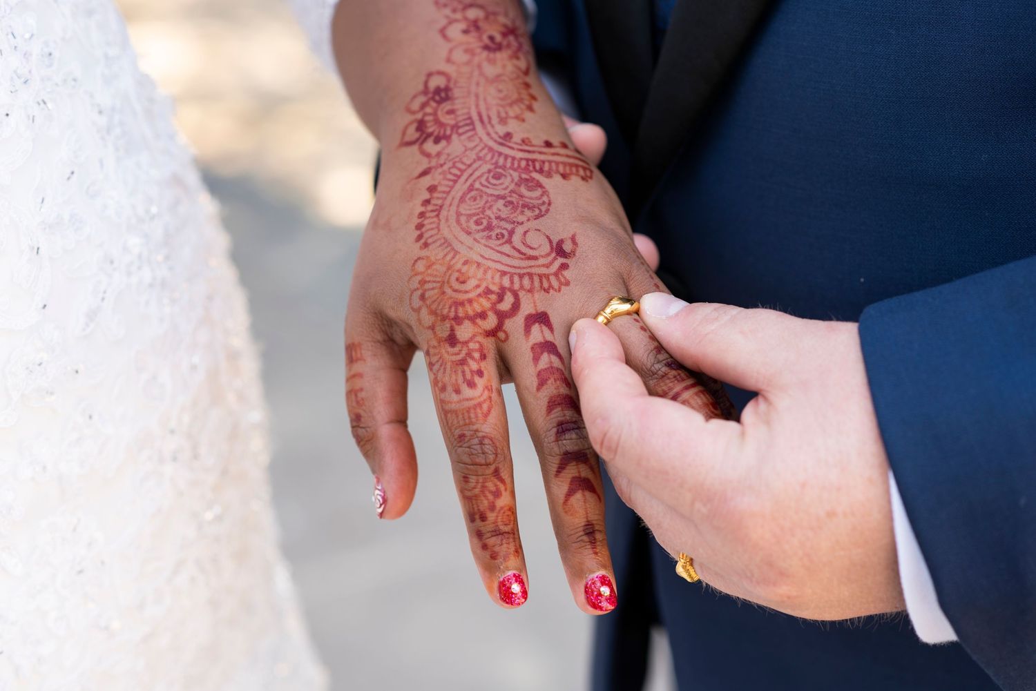A hand adorned with intricate henna designs receives a wedding ring during a ceremony.