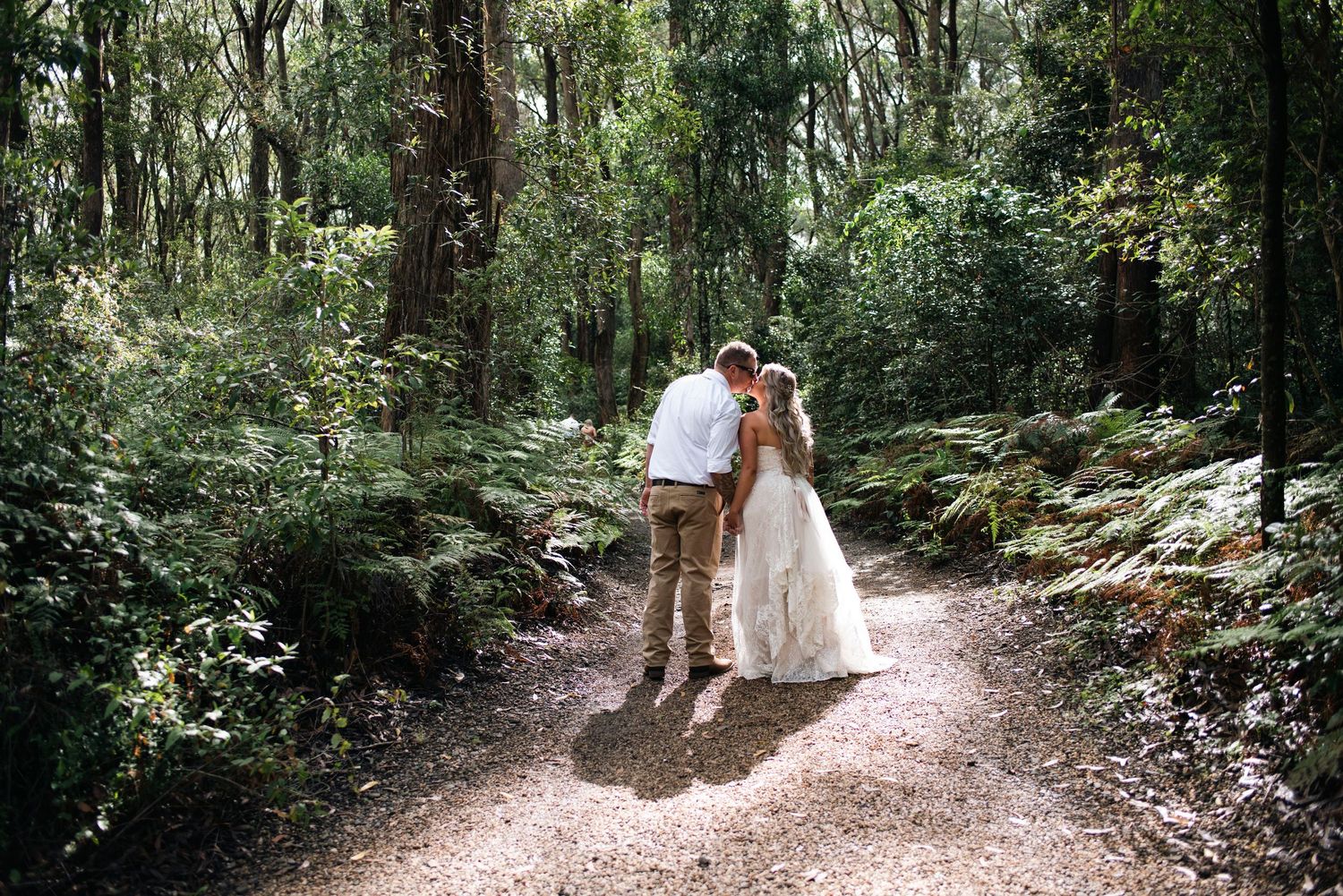A couple walking hand in hand down a forest path surrounded by lush greenery.