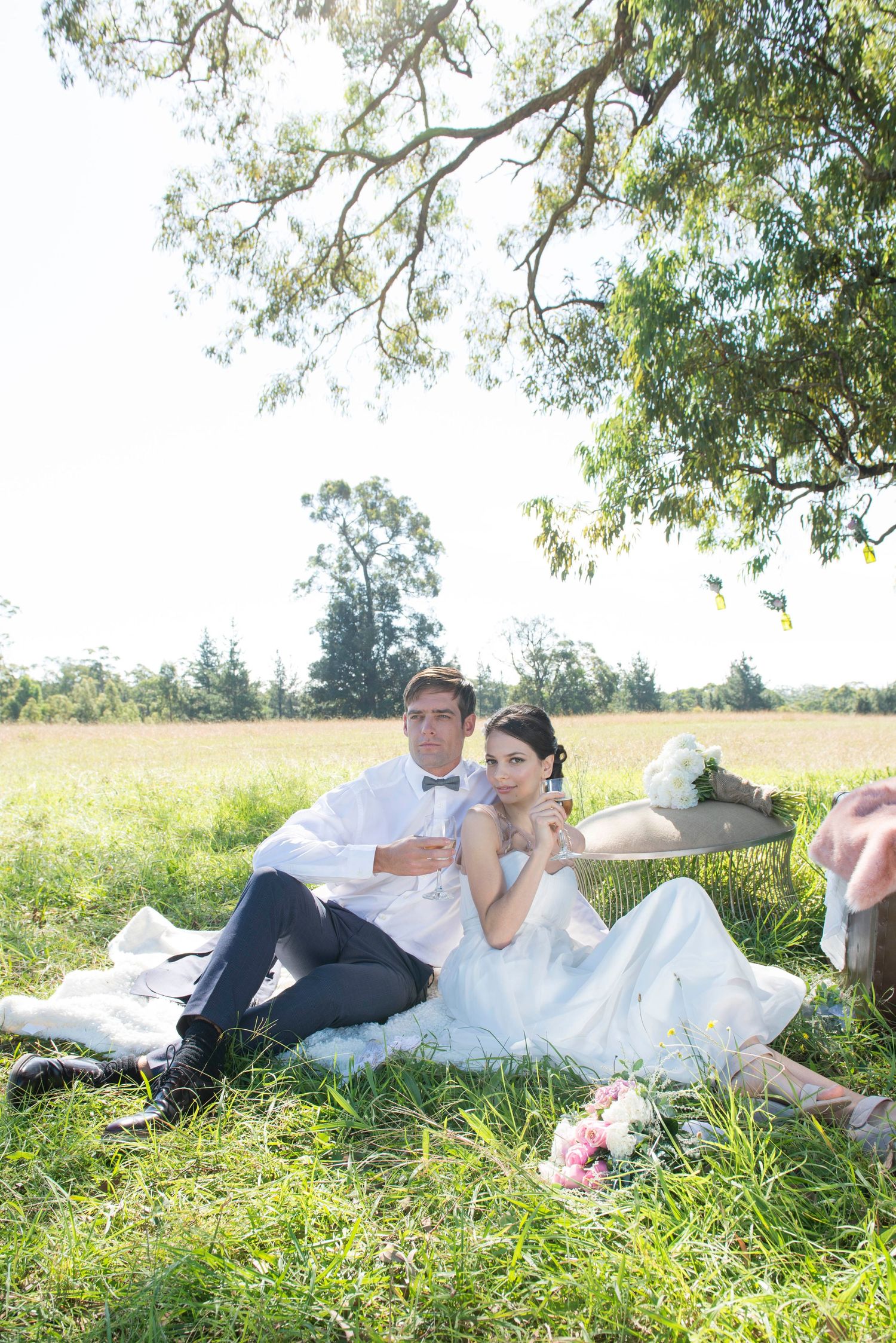 Wedding couple relaxing on blanket in sunny meadow during outdoor photoshoot.