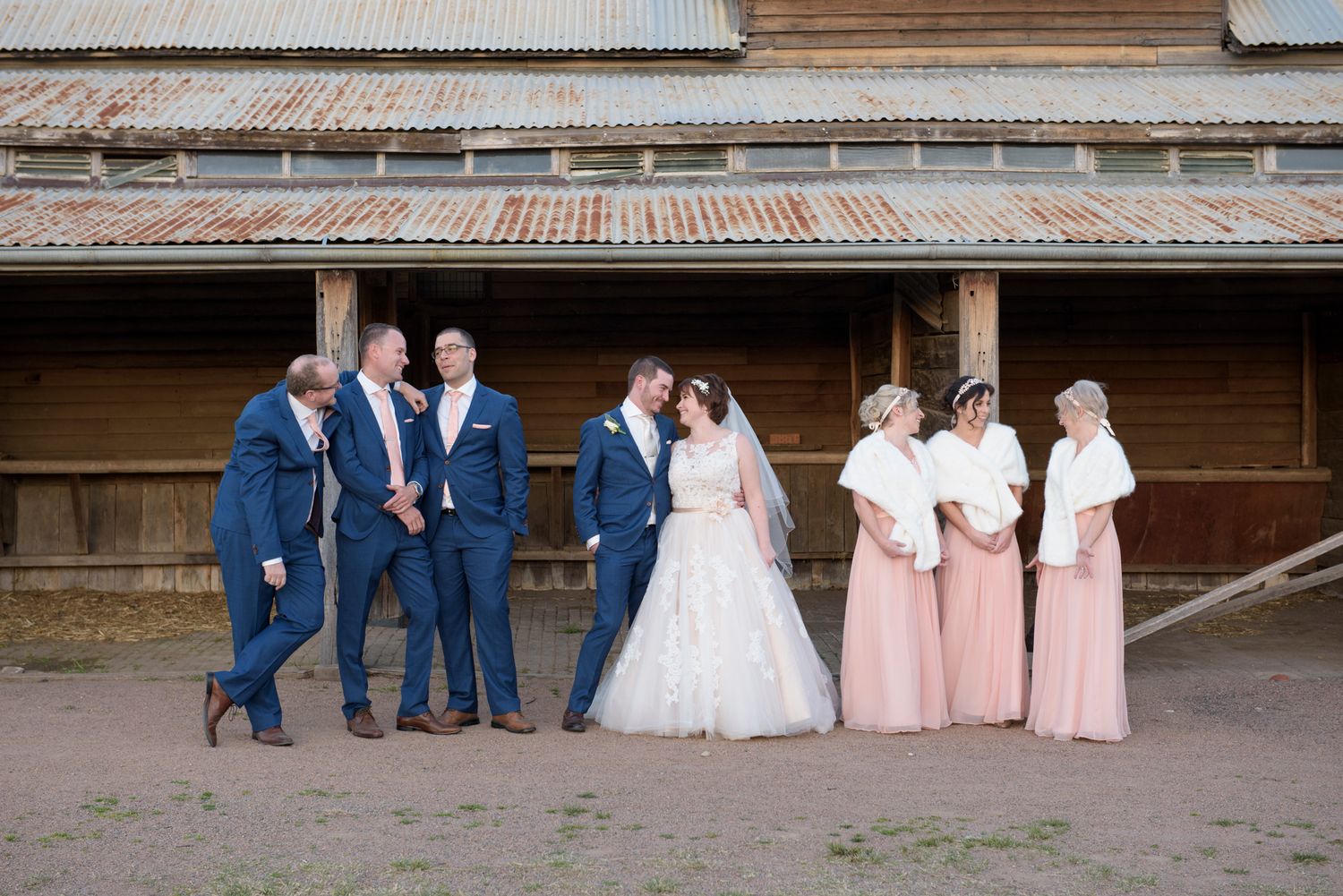 Wedding party members arranged in formal lineup against wooden backdrop.