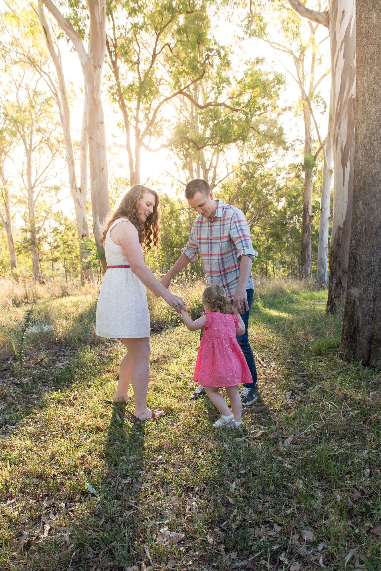 Family walks together through sunlit forest during golden hour photo session.