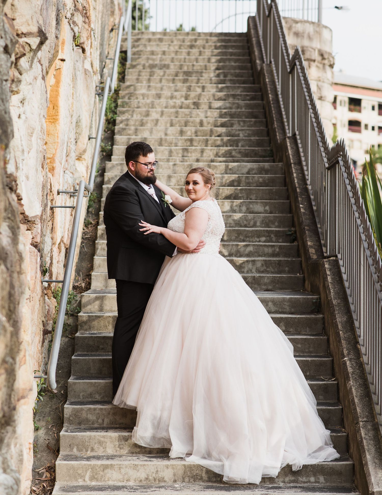 A bride and groom share romantic moments on a stone staircase surrounded by rustic architecture.