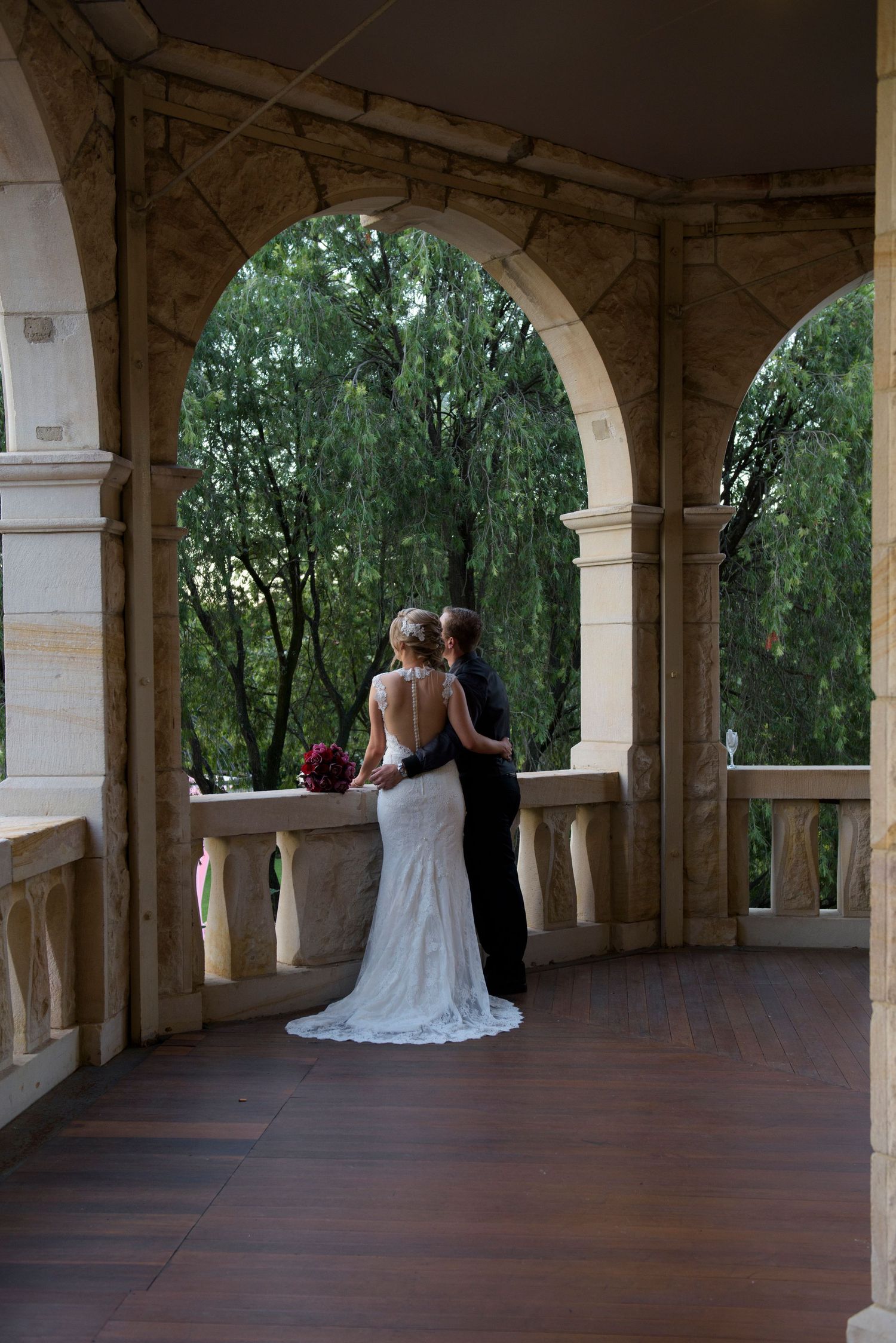 Wedding couple photographed under stone archways on covered porch.