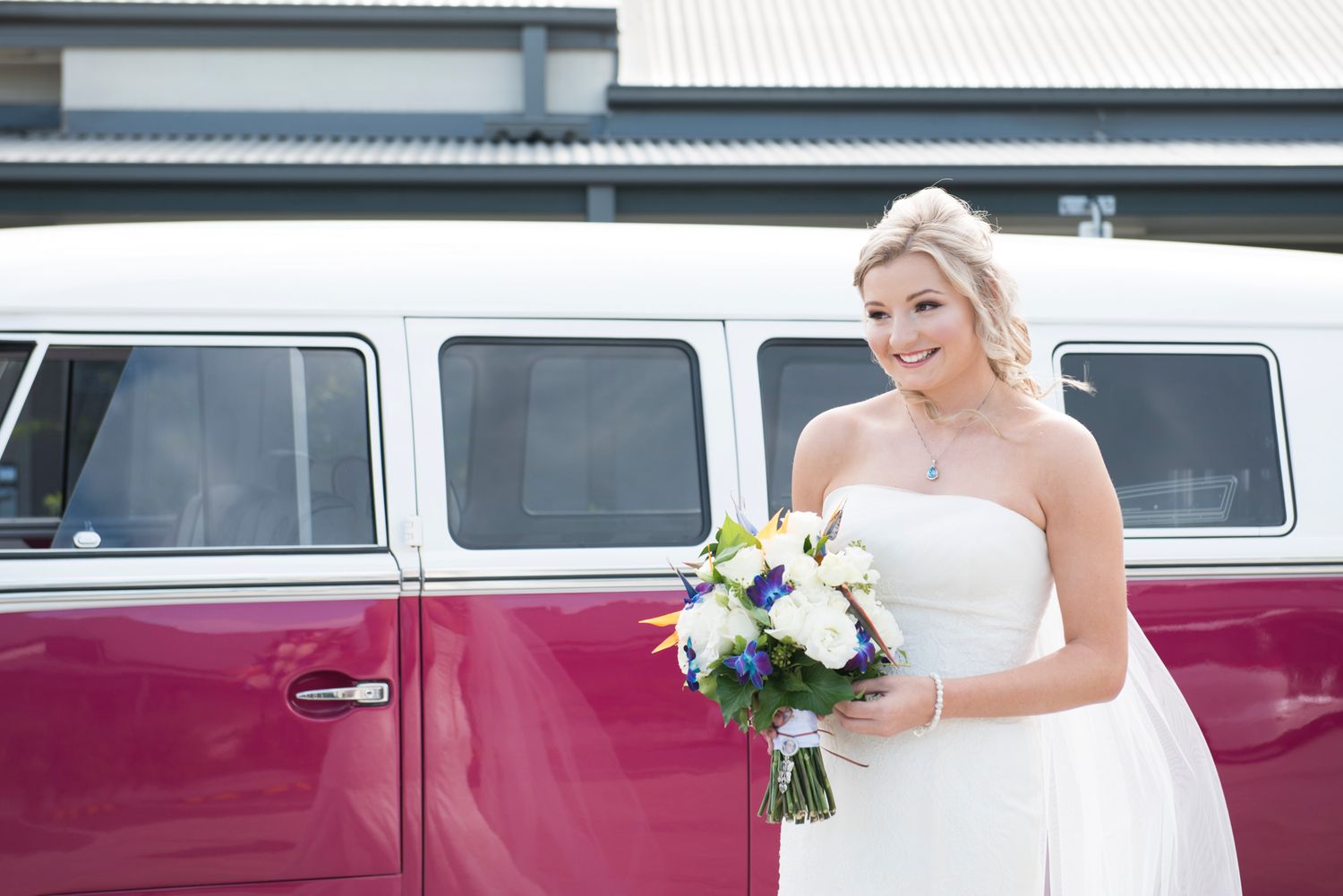Bride stands beside a vintage burgundy vehicle on their special day.