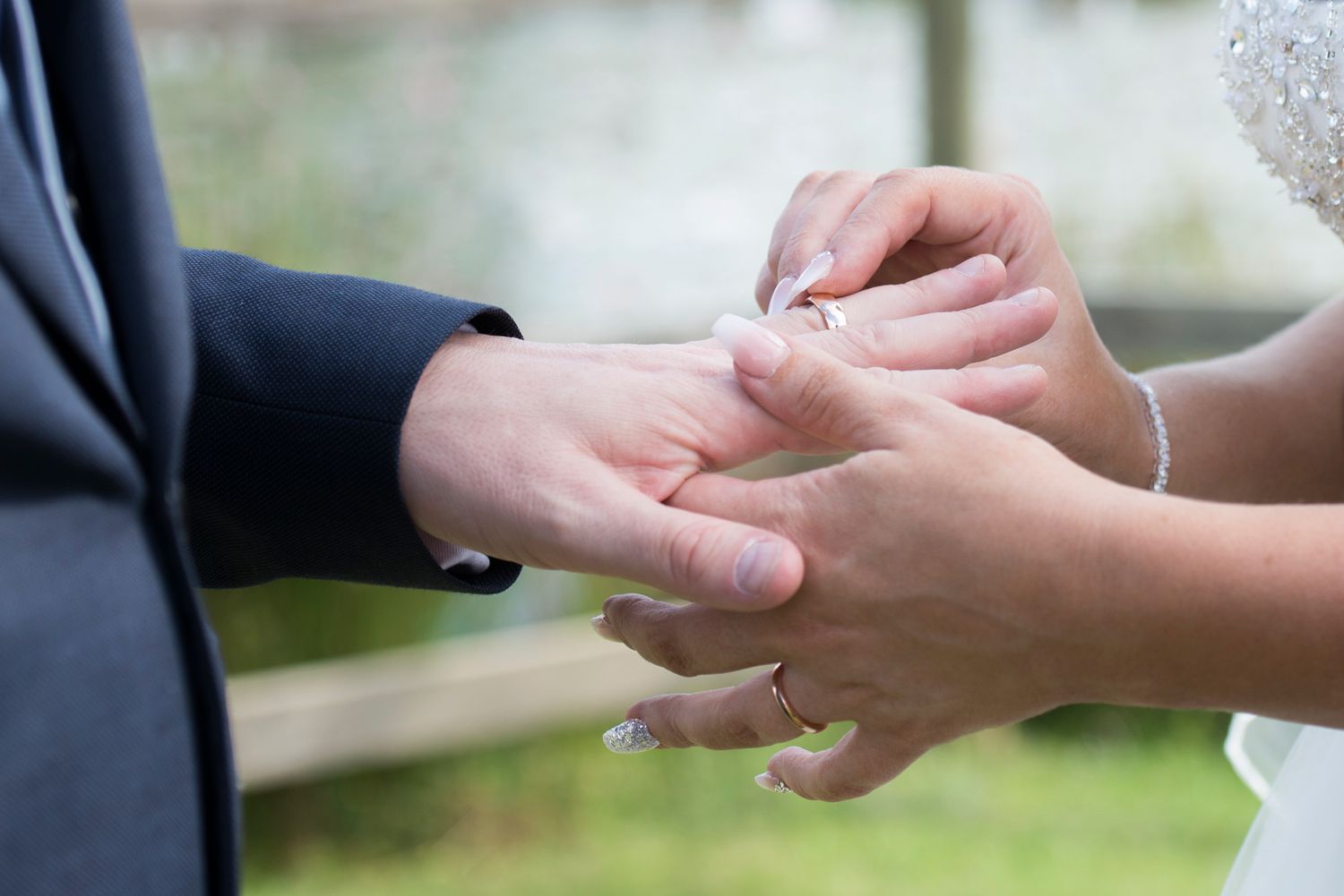Close up of hands exchanging wedding rings during an outdoor ceremony.