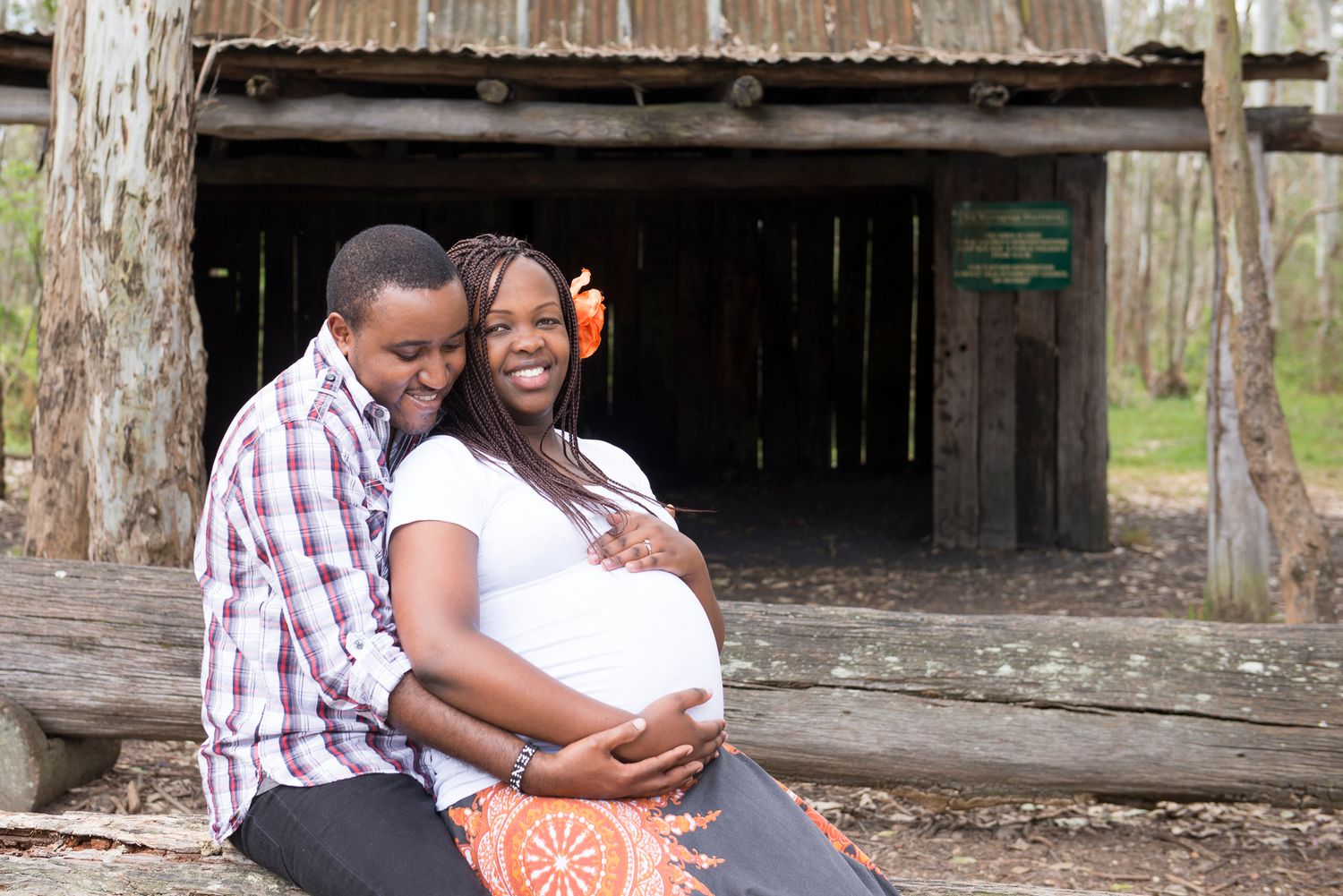 Expecting couple sharing a happy moment outdoors by rustic wooden structure.