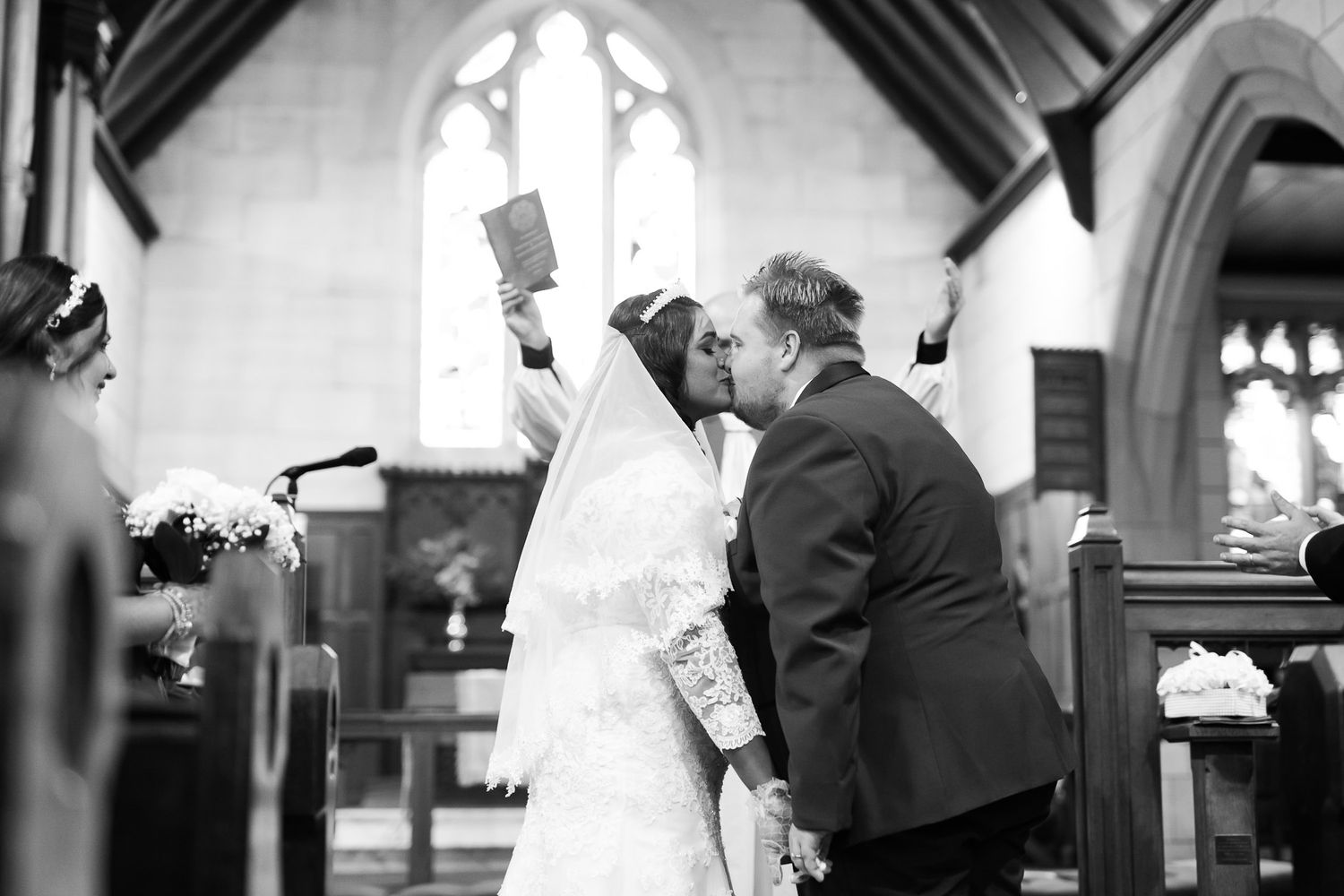 A romantic black and white wedding ceremony moment captured inside a beautiful church with gothic arched windows.