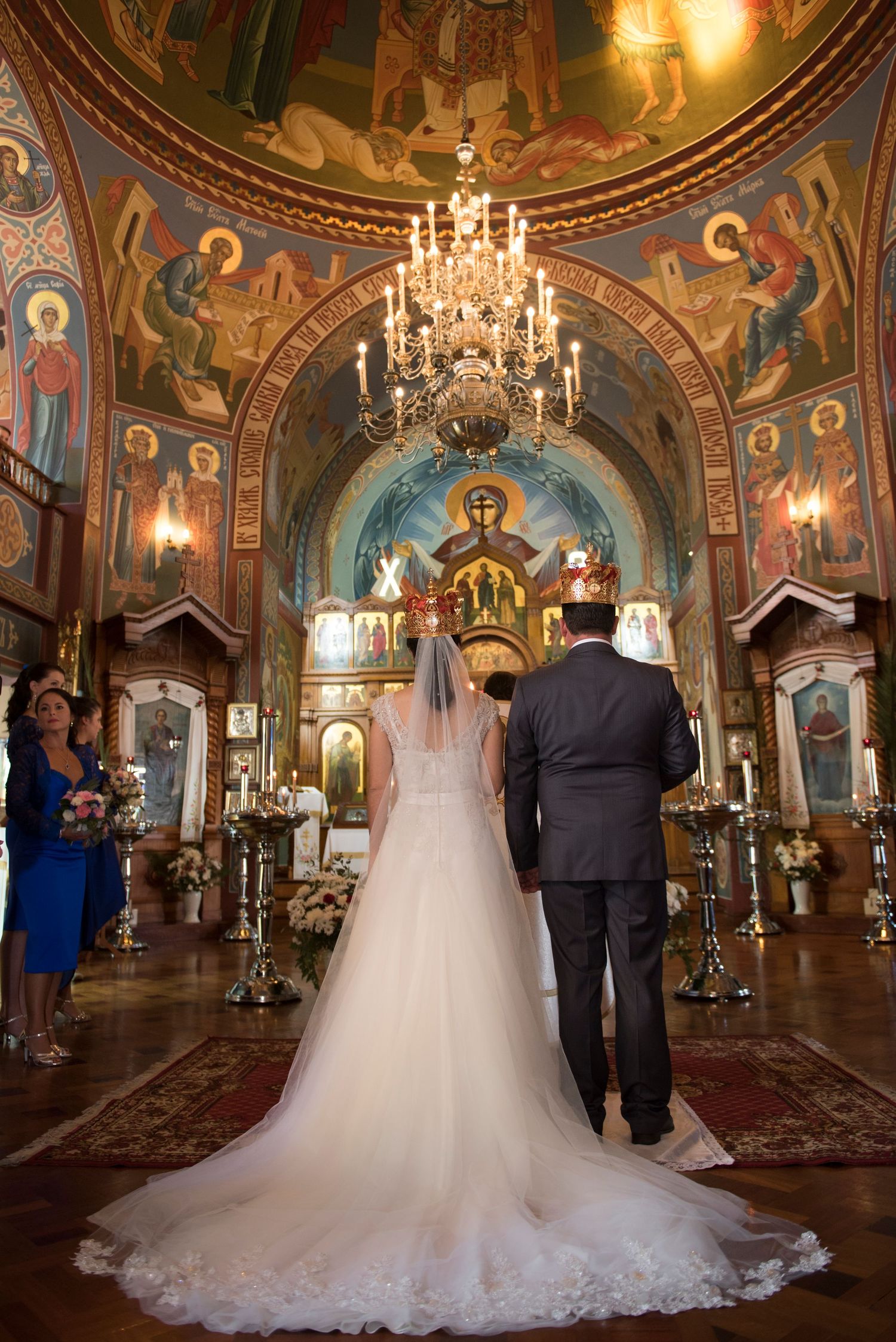 Wedding ceremony in a Russian Orthodox church with crystal chandeliers and detailed religious frescoes on the walls and ceiling.