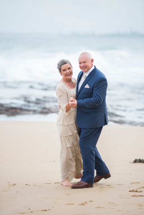 Bride and groom shares a romantic moment while walking together on a scenic beach at sunset.