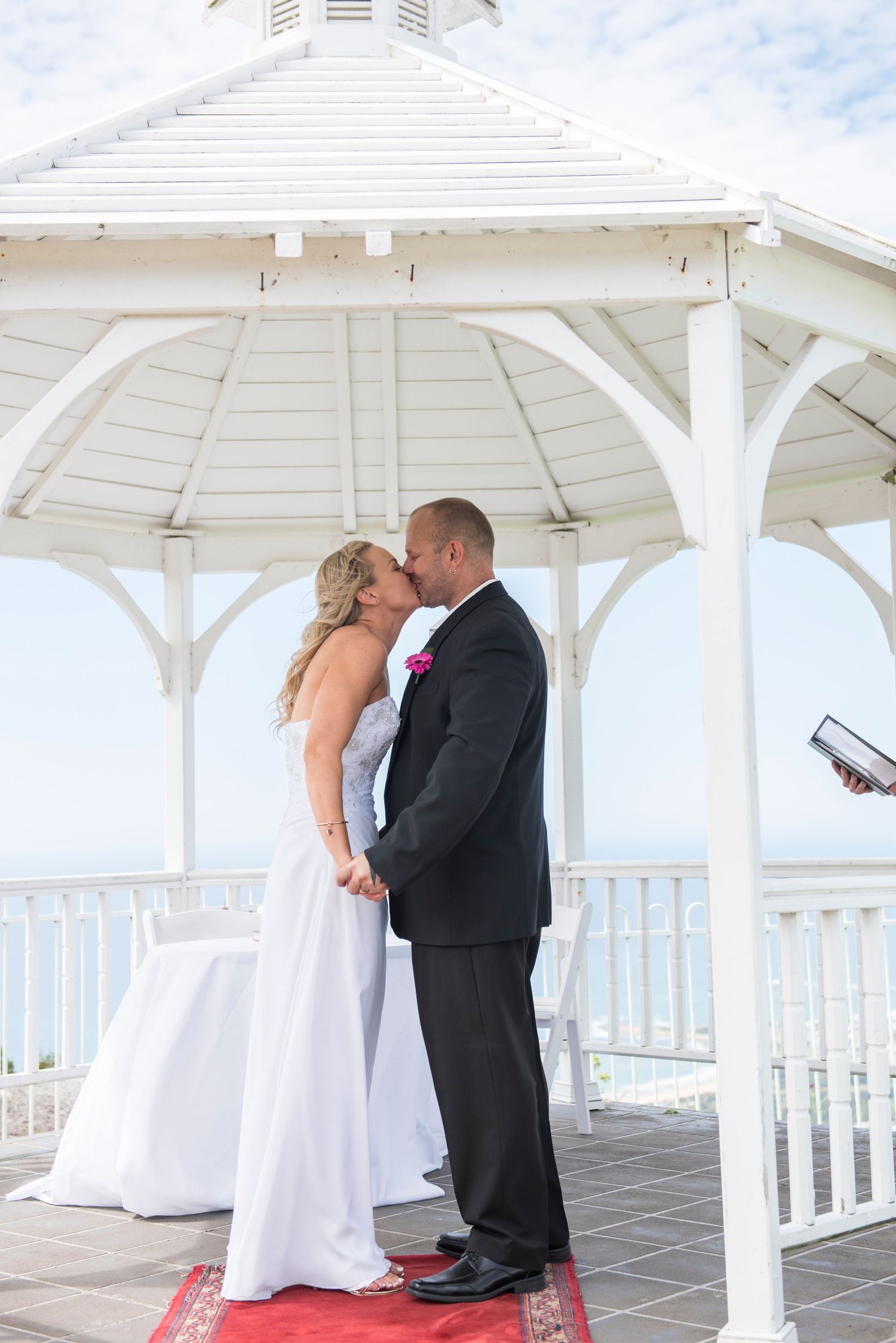 A couple shares an intimate moment under a white gazebo overlooking the beach on their wedding day at Panorama House.