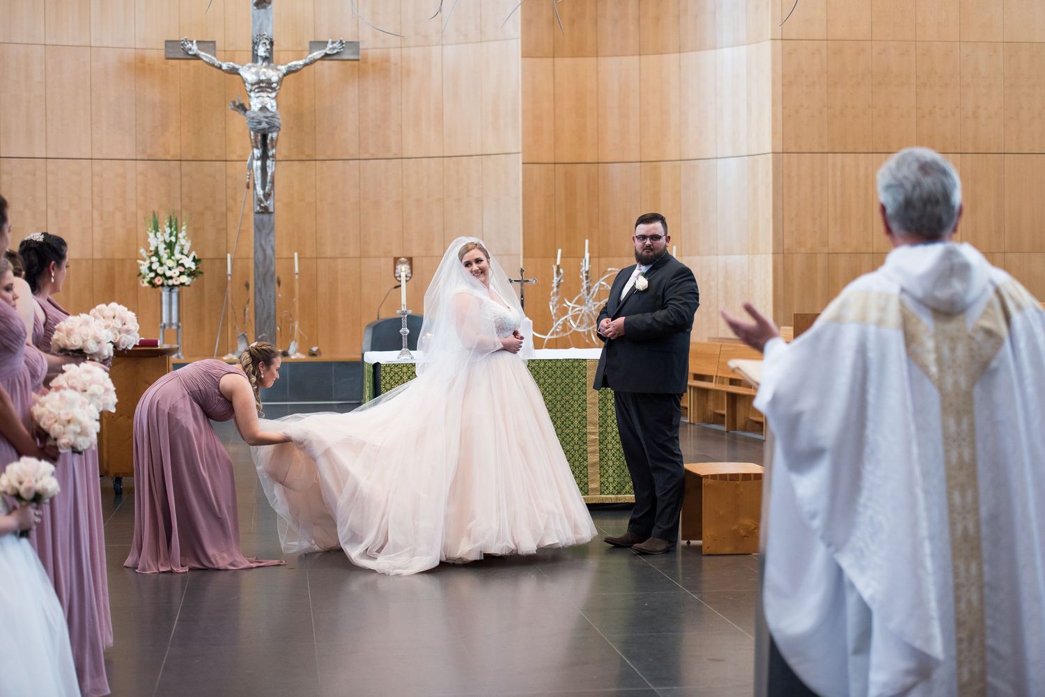 A Church wedding ceremony takes place and bridesmaid fixes brides dress.