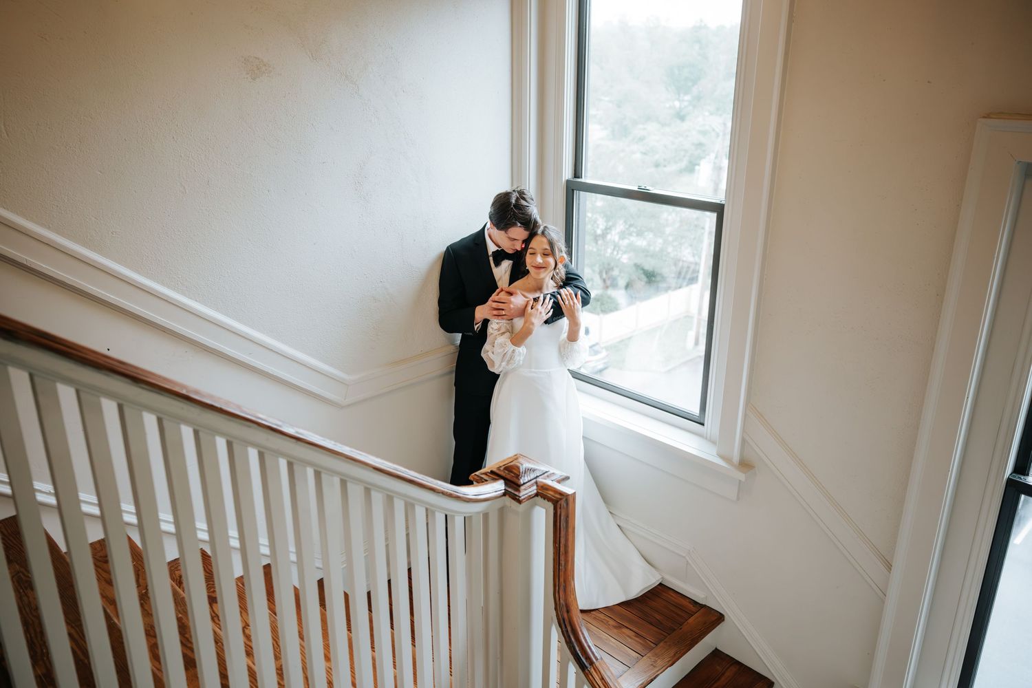 A couple embraces near a window with white railings in an indoor setting.