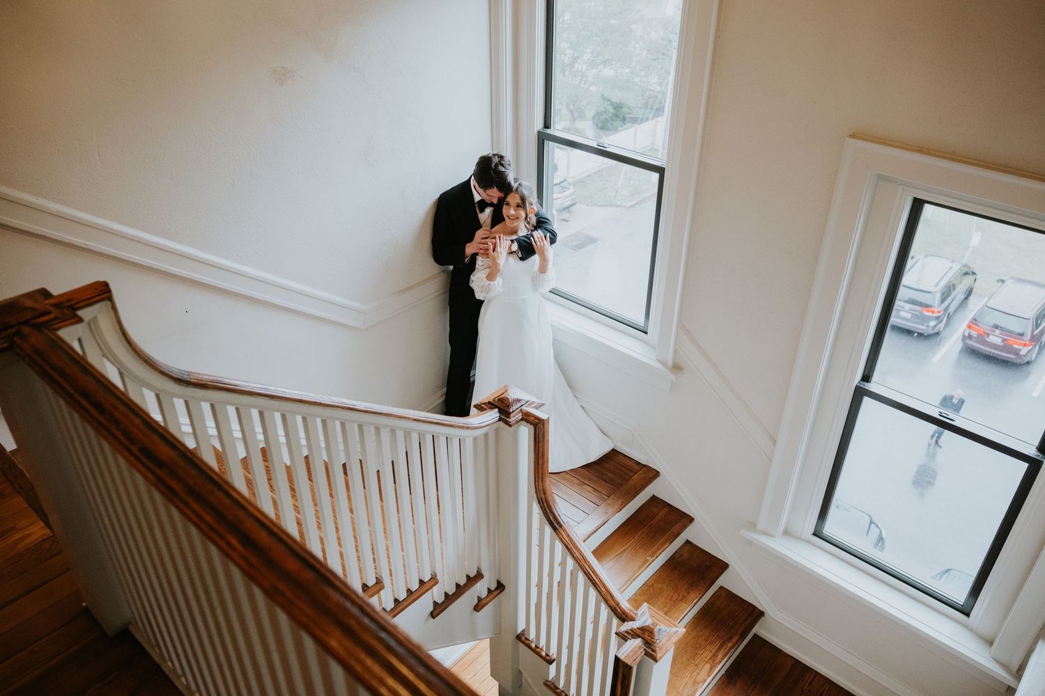 White painted stairwell with wooden banister and natural light from windows.