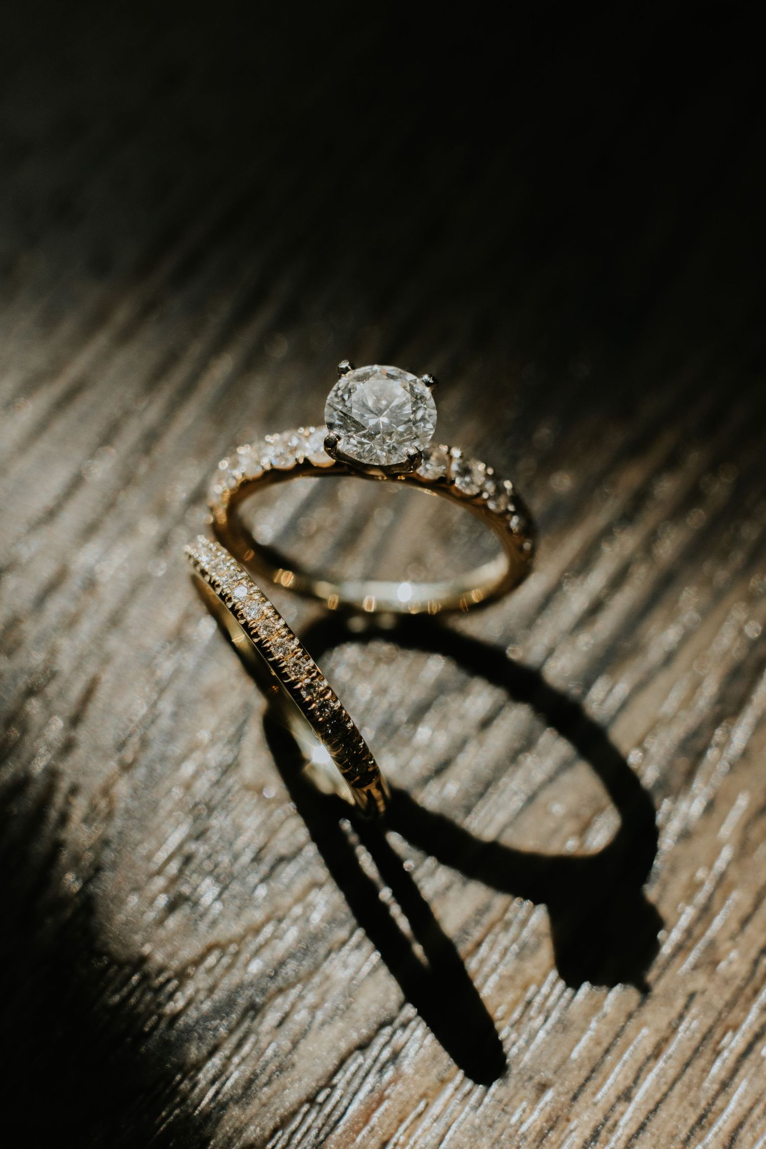 Wedding rings photographed with dramatic shadows on textured wooden surface.