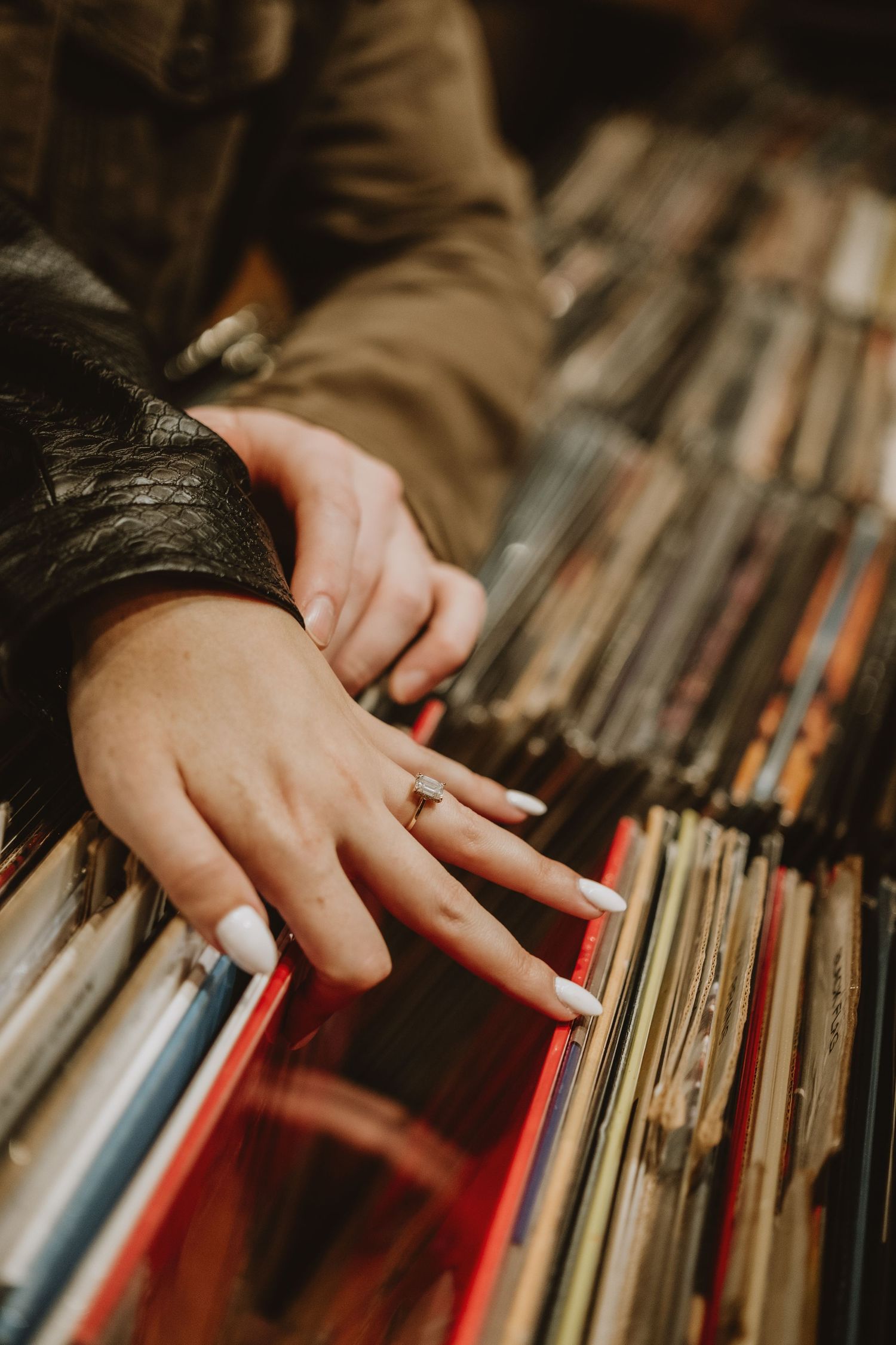 A hand browses through a collection of vinyl records on wooden shelves in warm lighting.