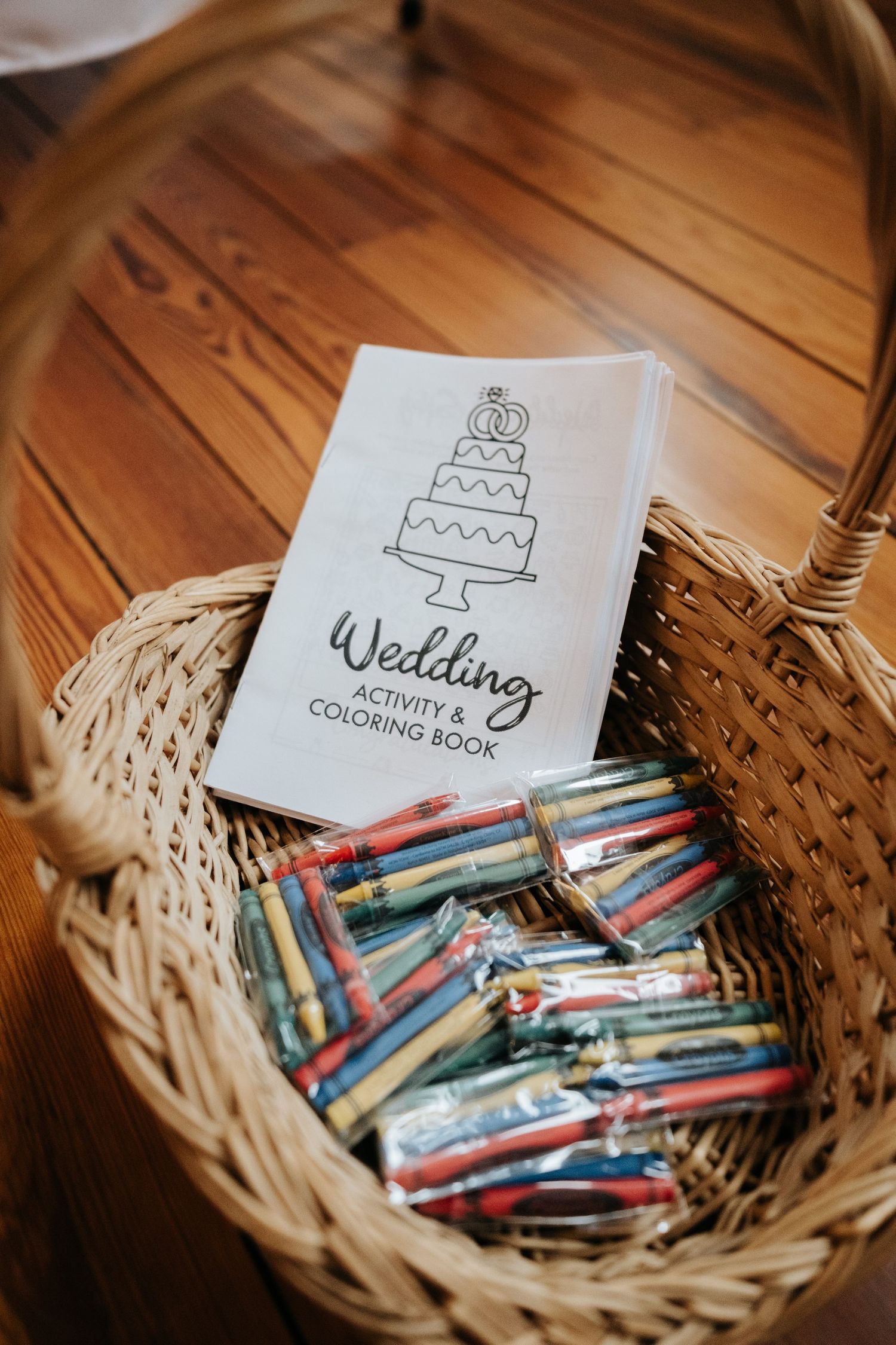 Wedding activity coloring books and colorful markers arranged in a woven basket on a wooden surface.