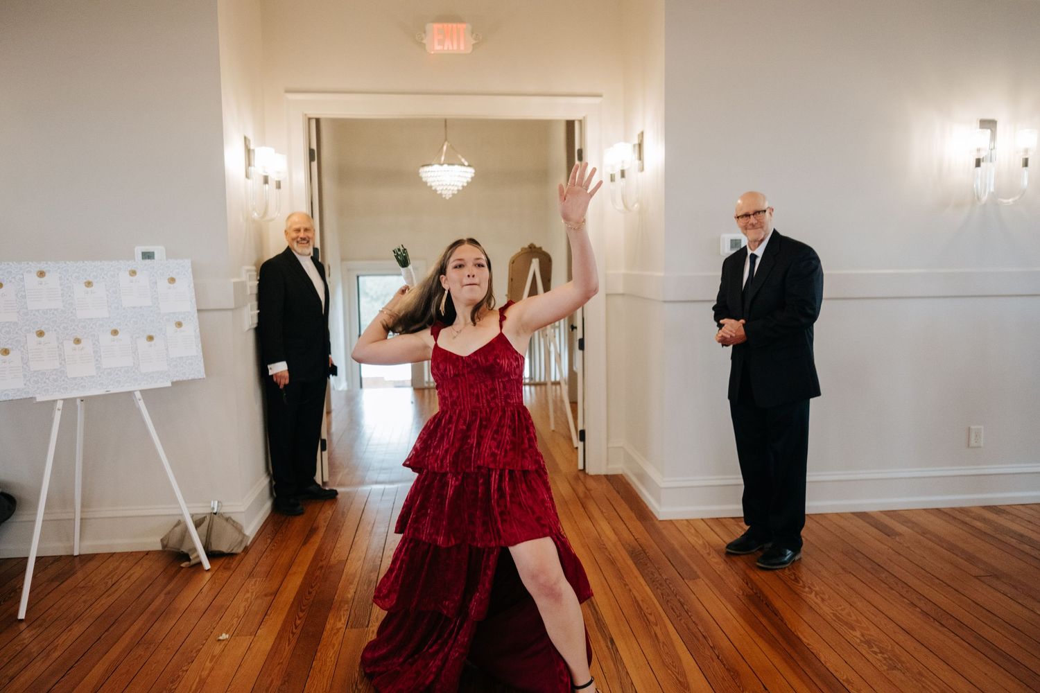 People dance and socialize in a bright ballroom space with wooden floors and string lights.